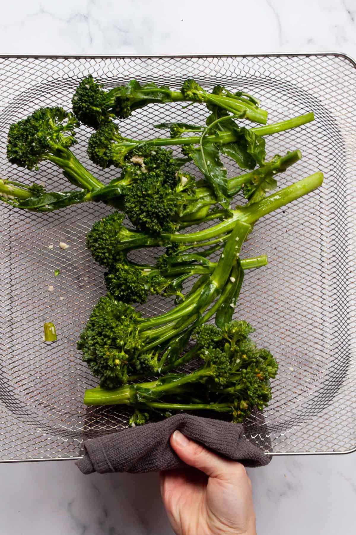 Seasoned broccolini arranged in a single layer in an air fryer basket.
