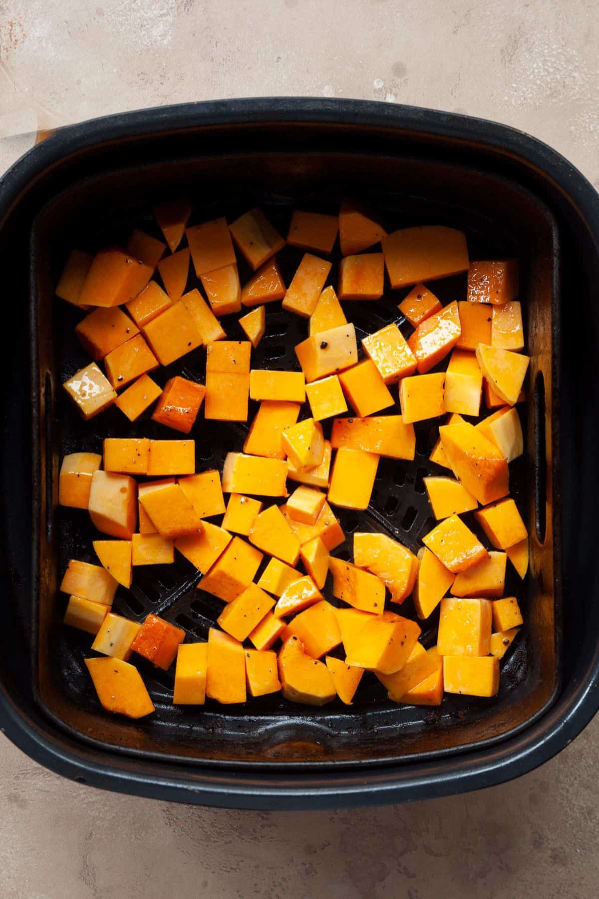 Seasoned raw butternut squash cubes spread in a single layer in a square air fryer basket.