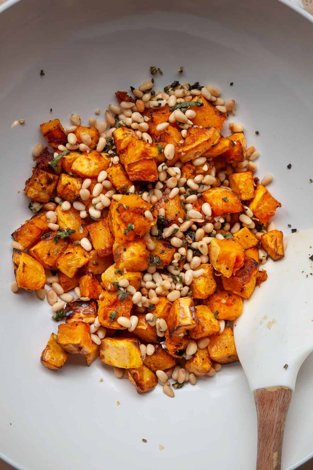 Air fried butternut squash cubes tossed with garlic, sage, and toasted pine nuts in a white bowl.