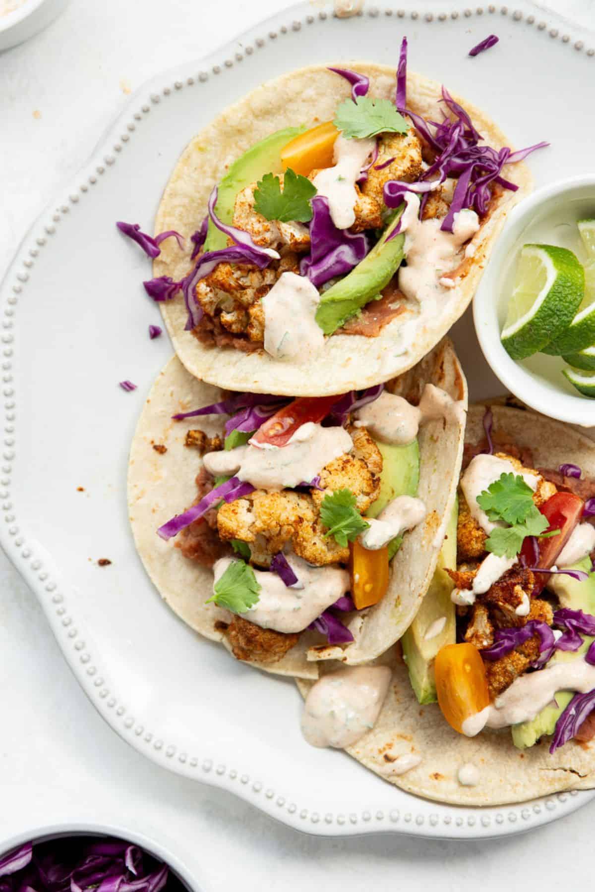 Three cauliflower tacos topped with red cabbage and yogurt crema on a plate.