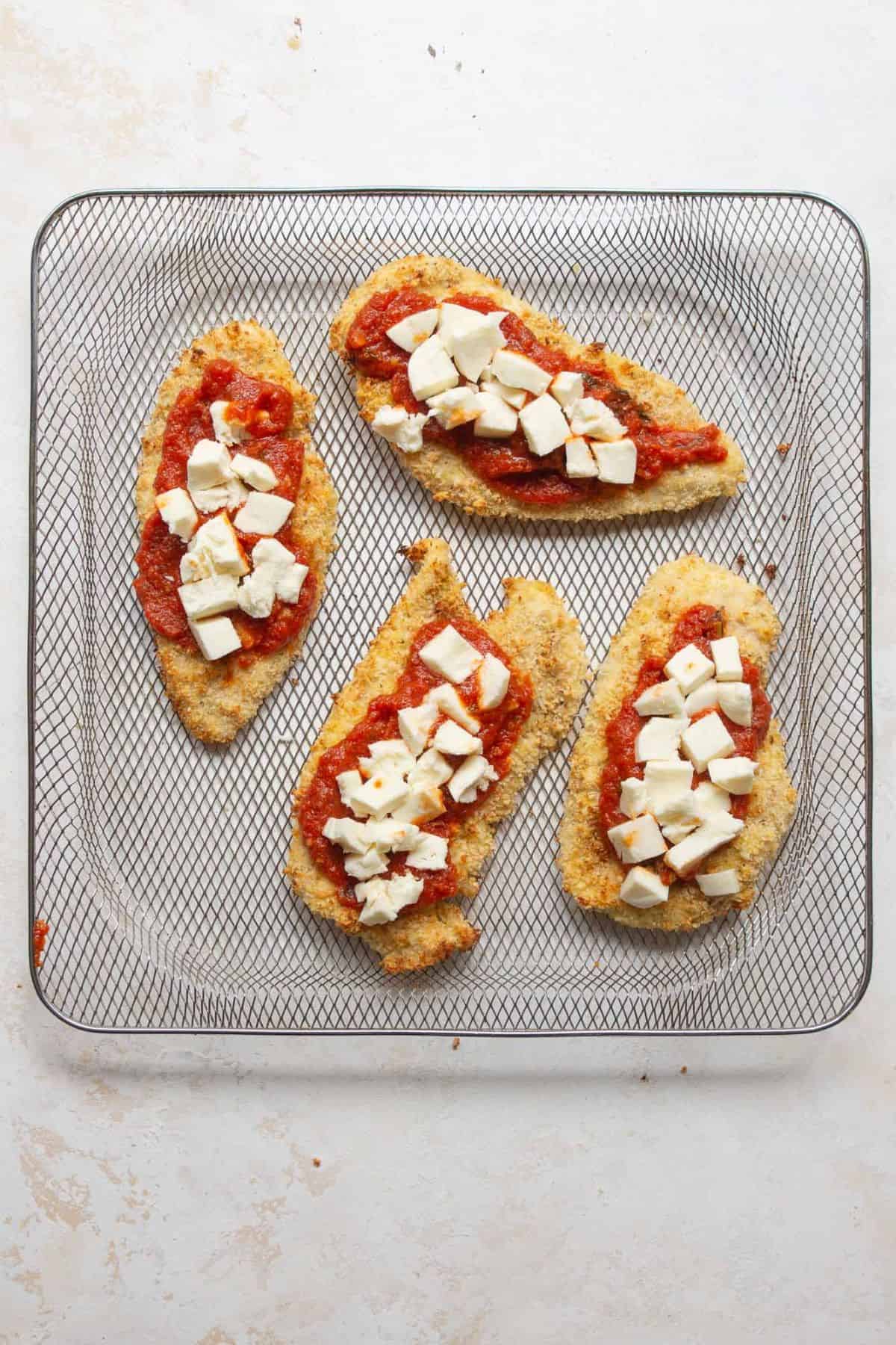 Crispy chicken cutlets topped with marinara and cubed fresh mozzarella in an air fryer basket.