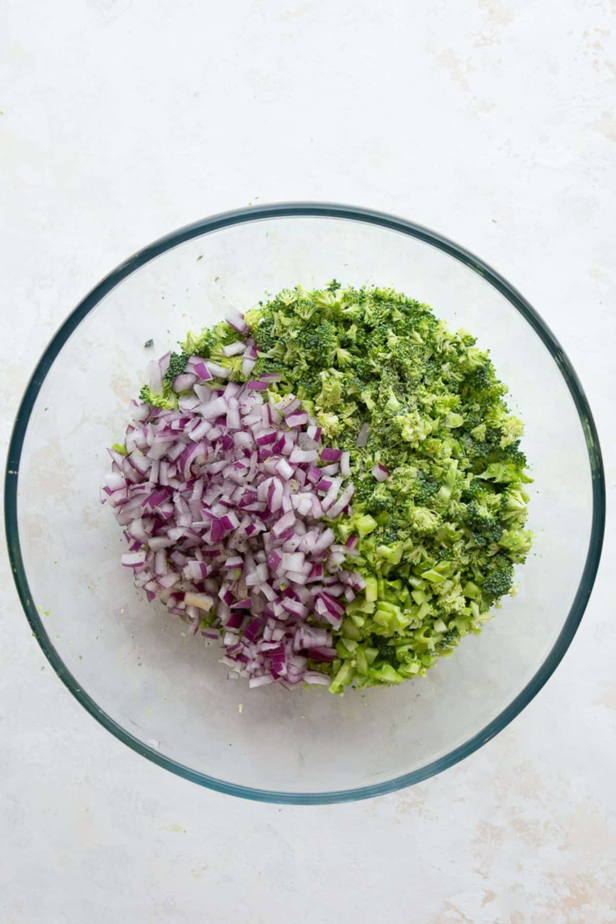 Finely chopped broccoli and diced red onion in a glass mixing bowl.