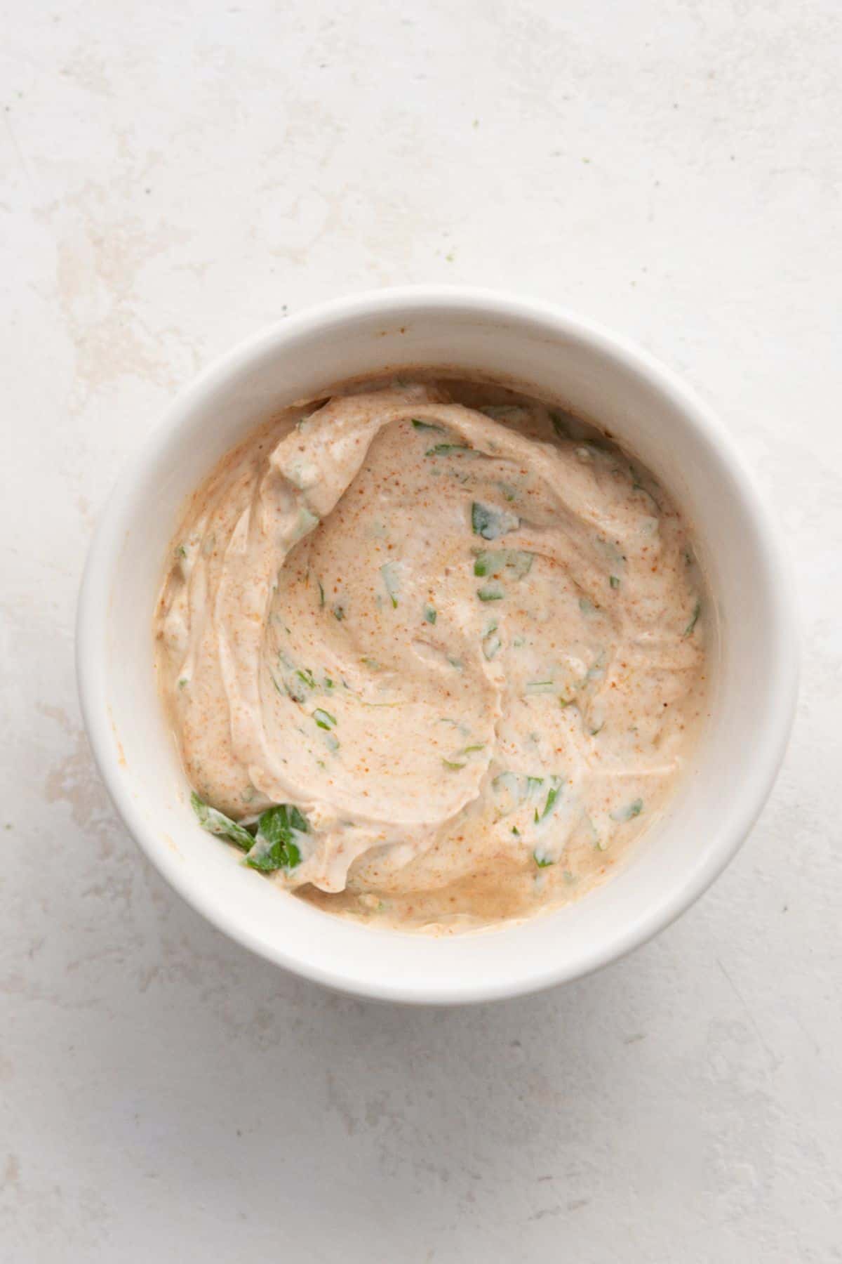 Cilantro yogurt crema with chili powder and chopped cilantro in a small white bowl.