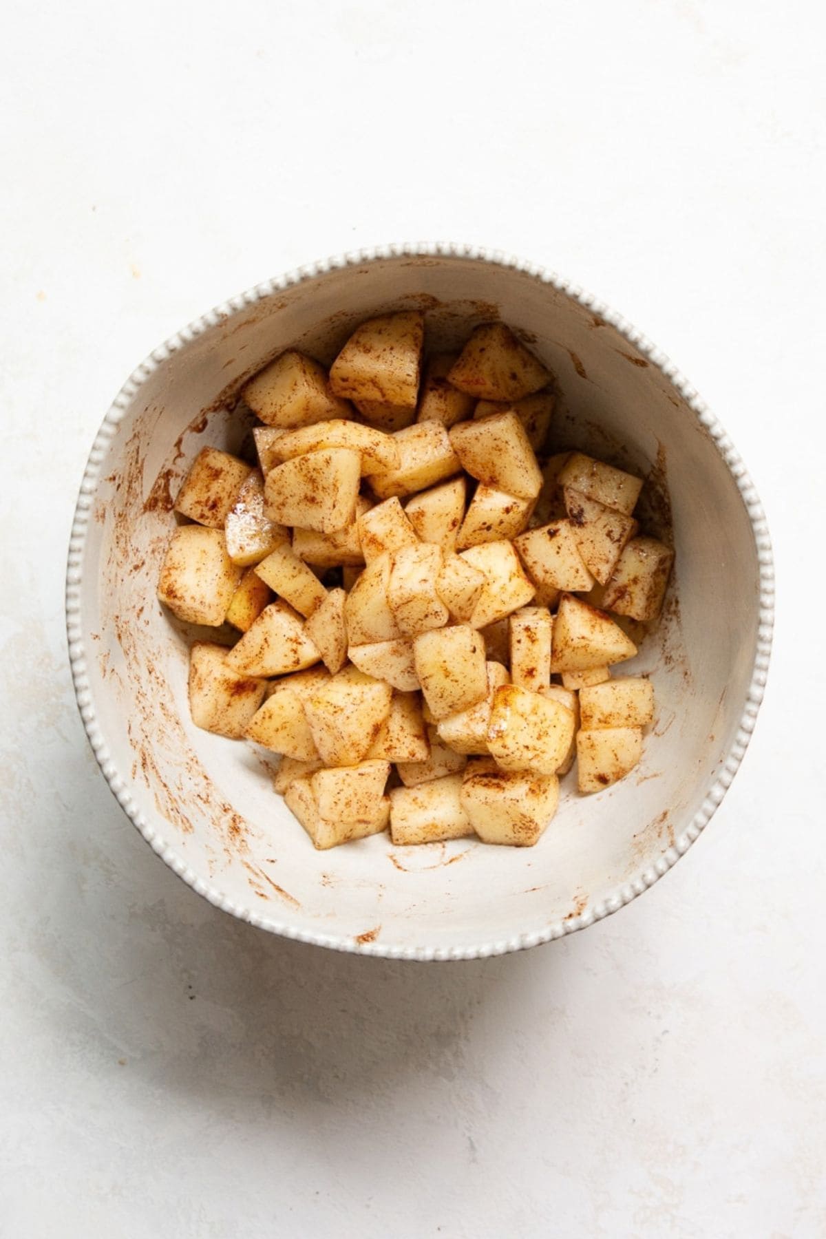 Apple cubes tossed with cinnamon, coconut oil, and maple syrup in a bowl.