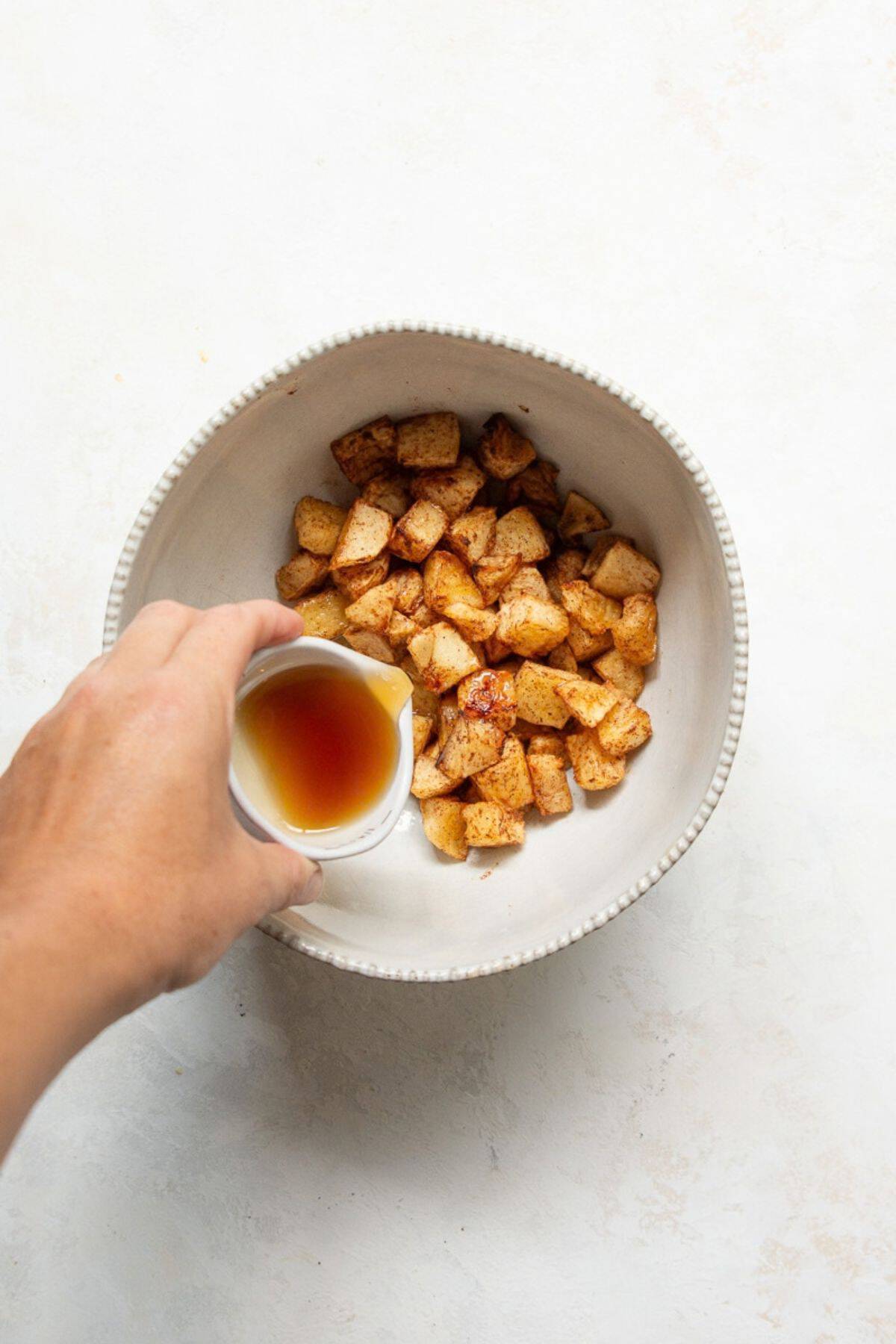 Pouring maple syrup over warm air fryer apples in a bowl for the final glaze.