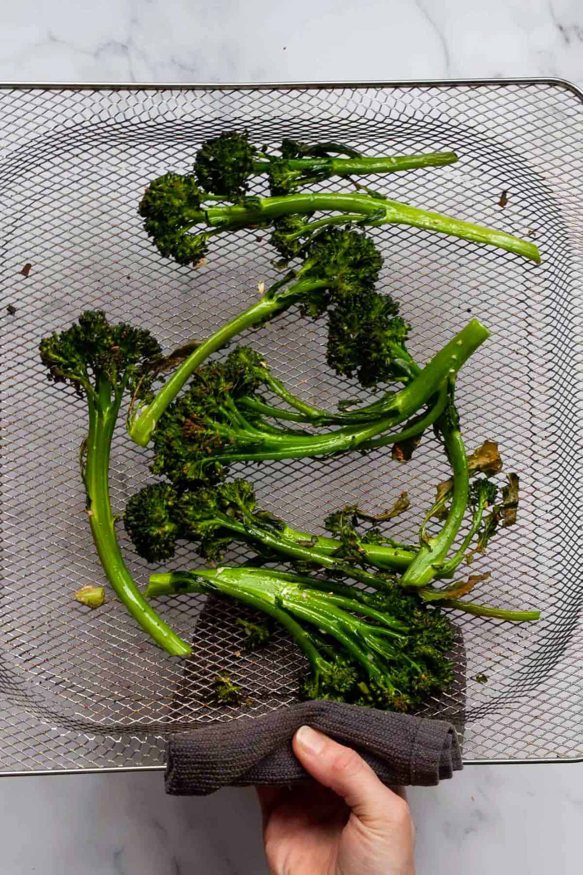 Crispy air fryer broccolini with charred tips in the air fryer basket.