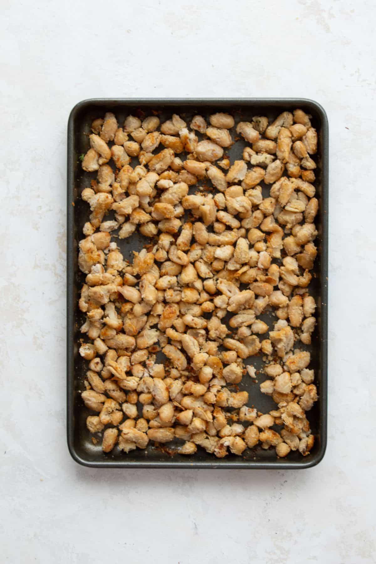 Crispy roasted white beans, golden and crumbled, on a sheet pan.