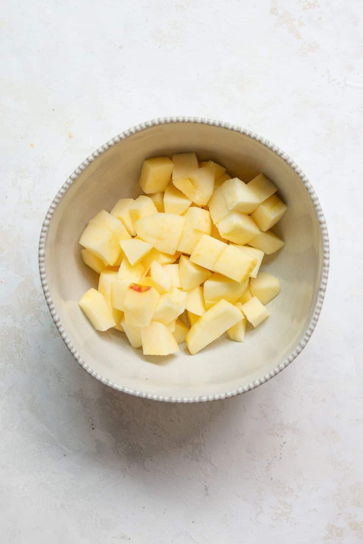 Peeled apples cut into 1-inch cubes in a white bowl.