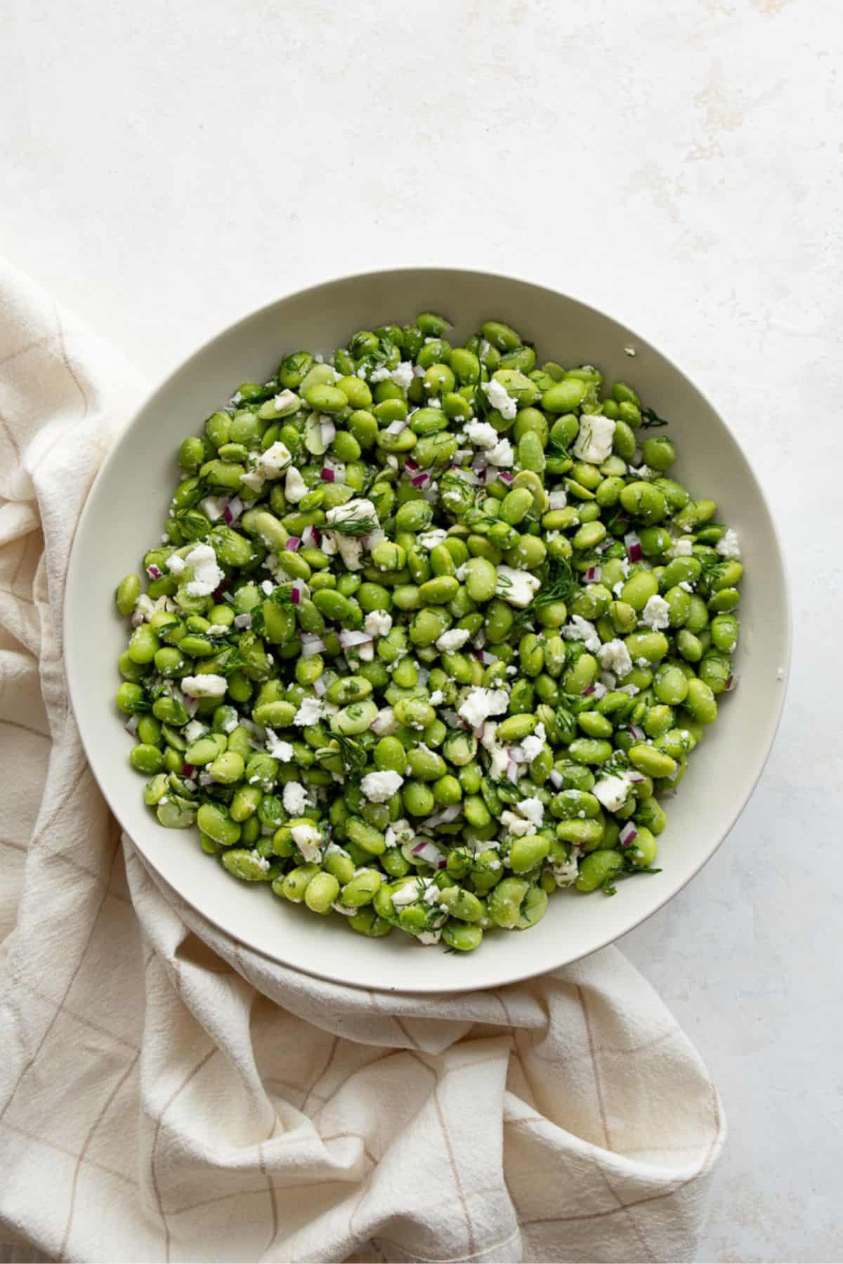 Overhead view of tossed edamame salad with feta and dill in a large bowl.