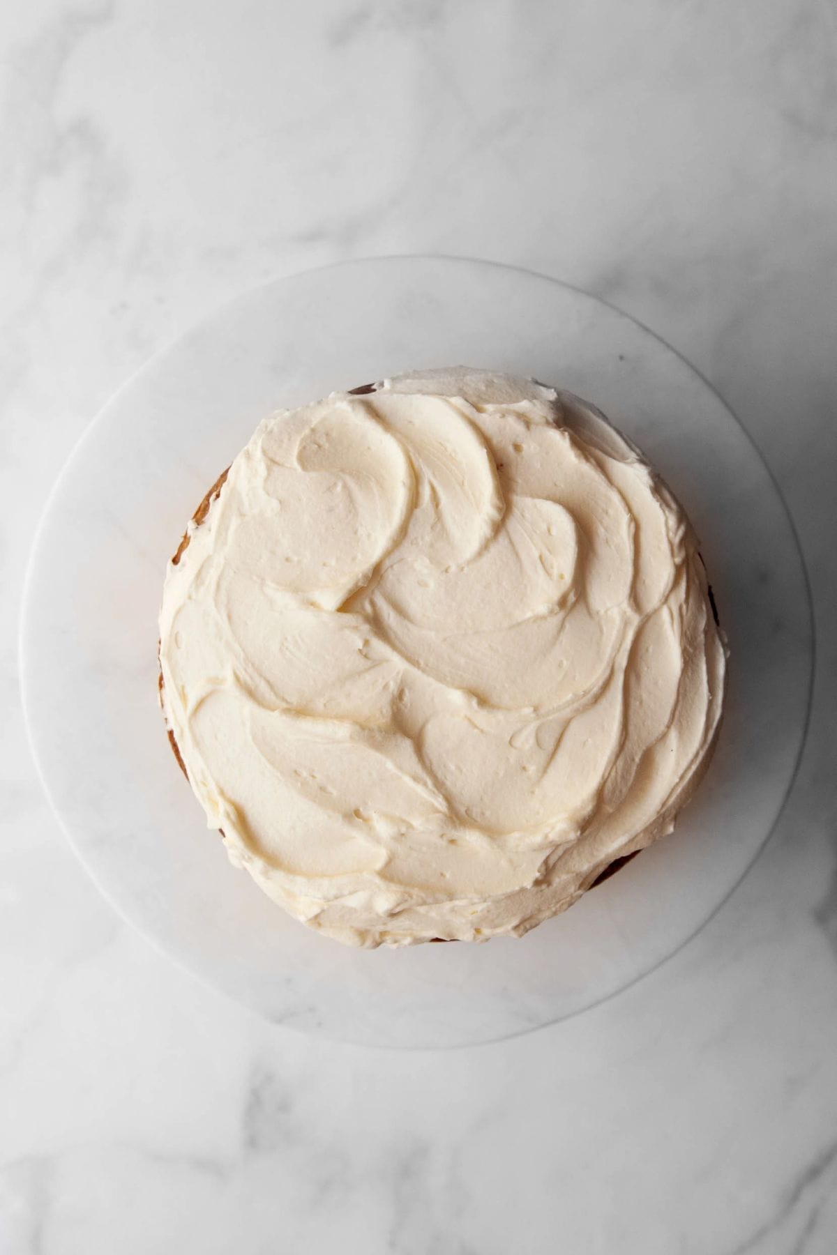 Cooled pumpkin carrot cake layer topped with a swirl of Greek yogurt cream cheese frosting on a cake plate.