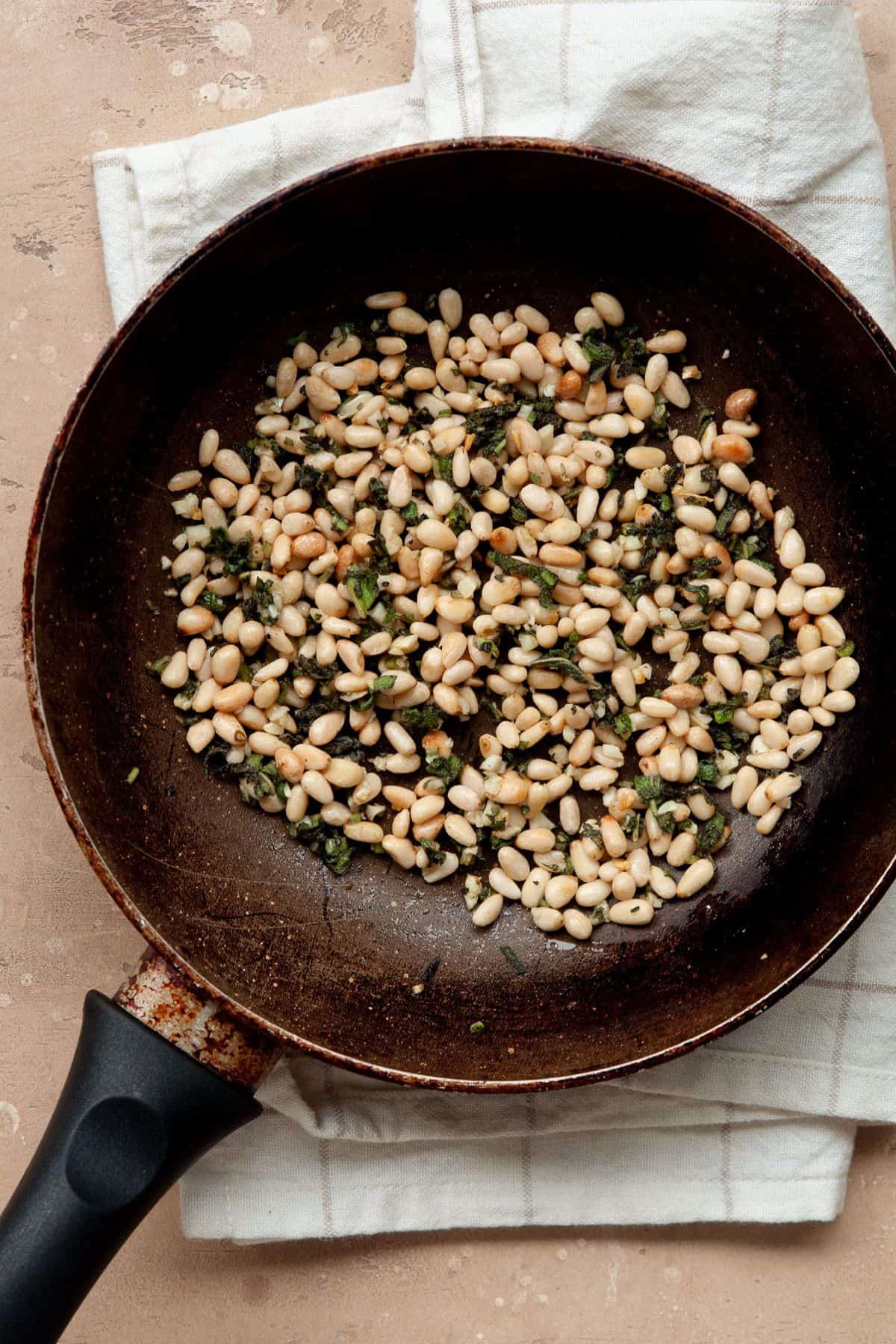 Toasted pine nuts with minced garlic and fresh sage in a small skillet.