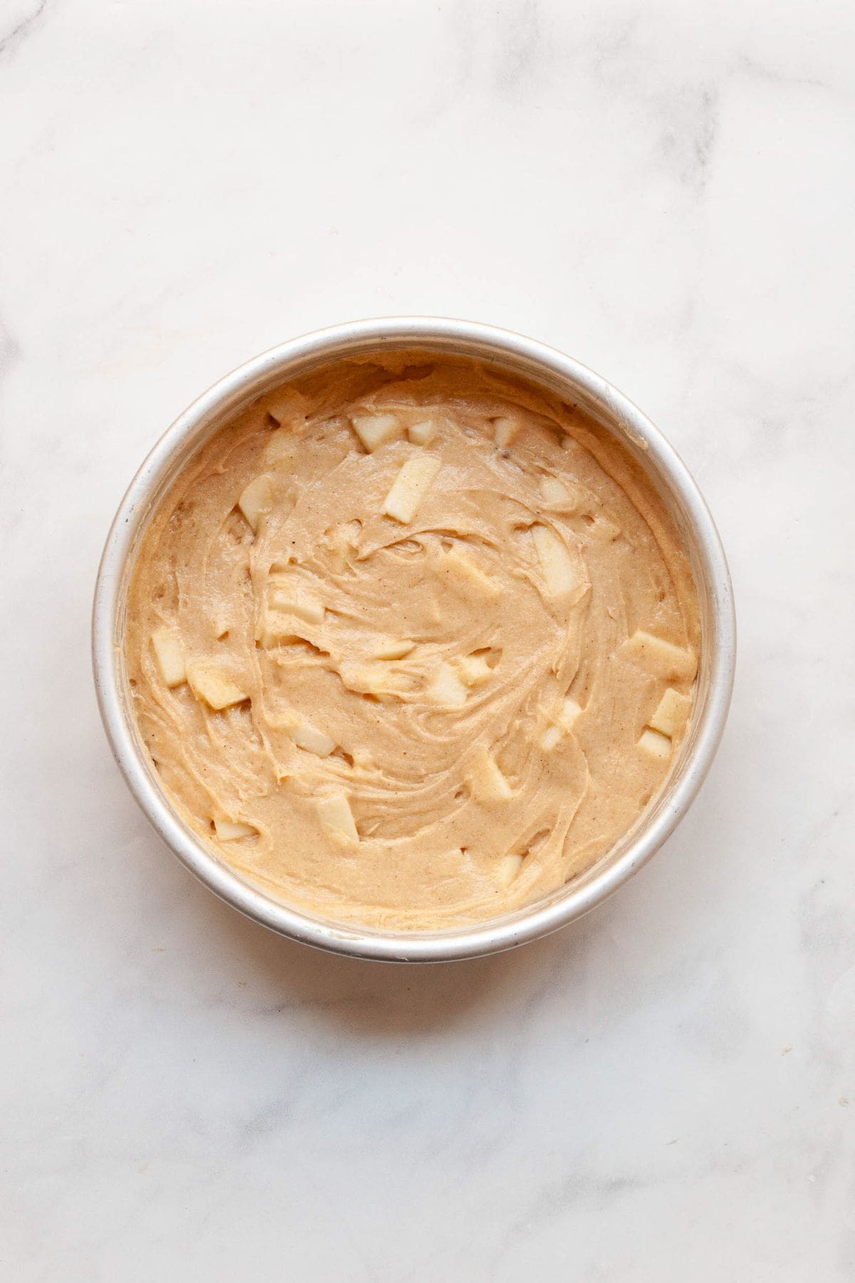 Gluten-free apple cake batter spread evenly in a round cake pan before baking.