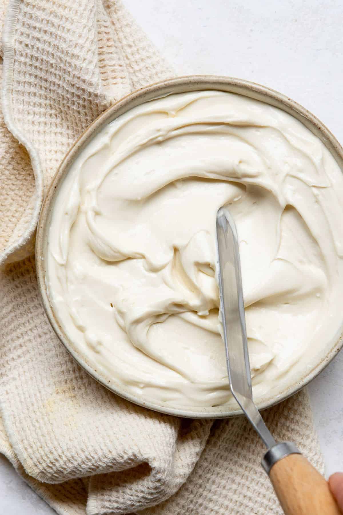 Whipped Greek yogurt cream cheese frosting in a mixing bowl with a spatula.