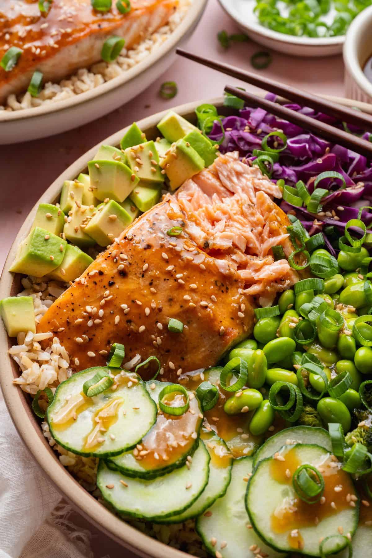 Flaky teriyaki-glazed salmon in a healthy bowl with avocado, edamame, red cabbage, and cucumber.