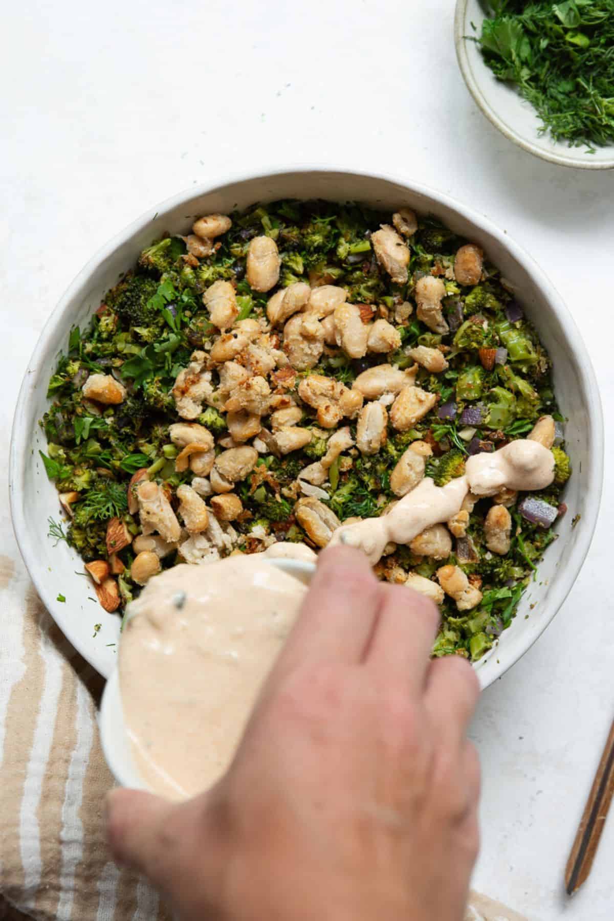 Lemon yogurt dressing being poured over roasted broccoli salad.