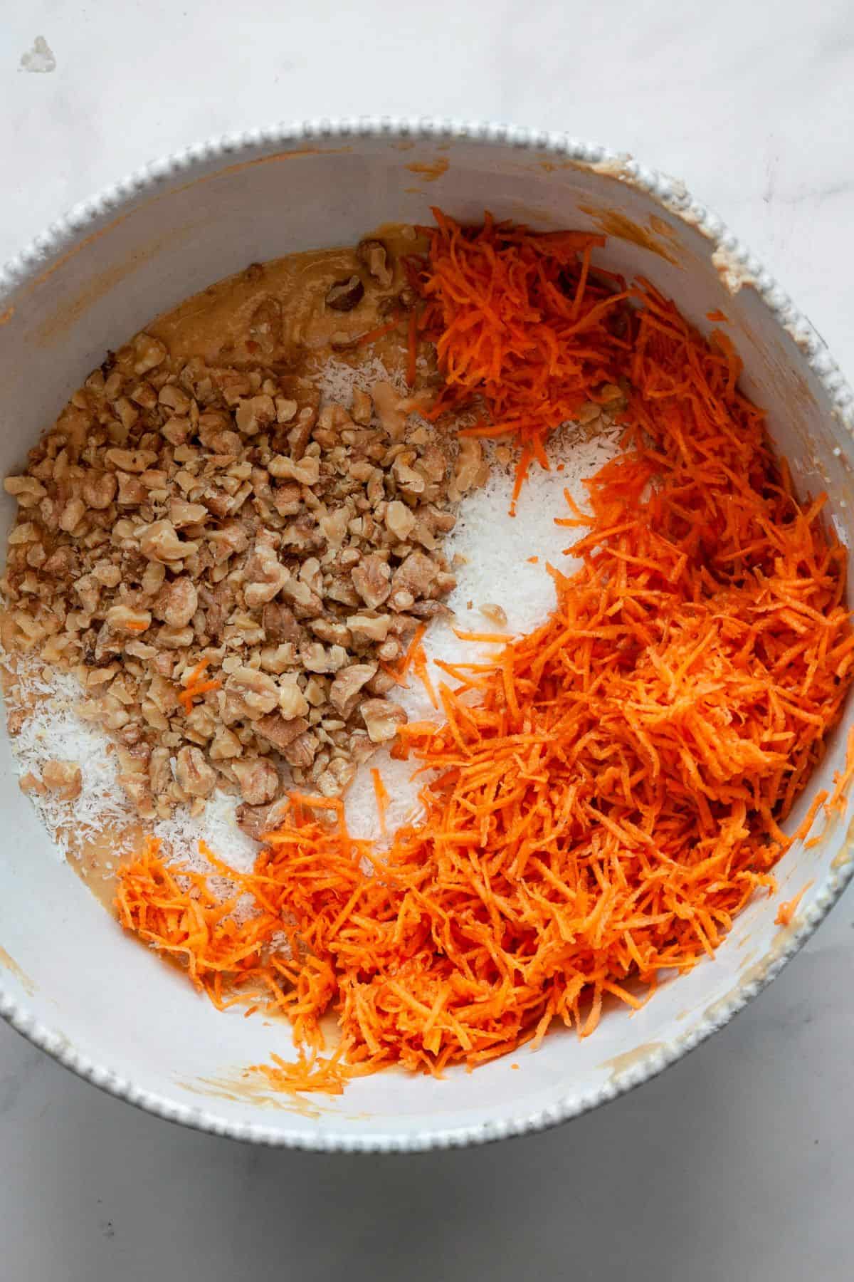 Pumpkin carrot cake batter in a mixing bowl with grated carrots and chopped walnuts on top, ready to fold in.