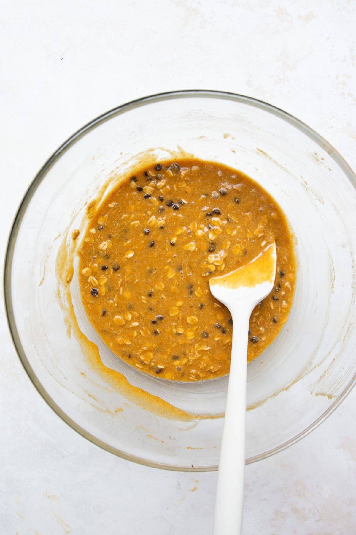 Pumpkin oatmeal bar batter with chocolate chips folded in, in a glass bowl with a spatula.