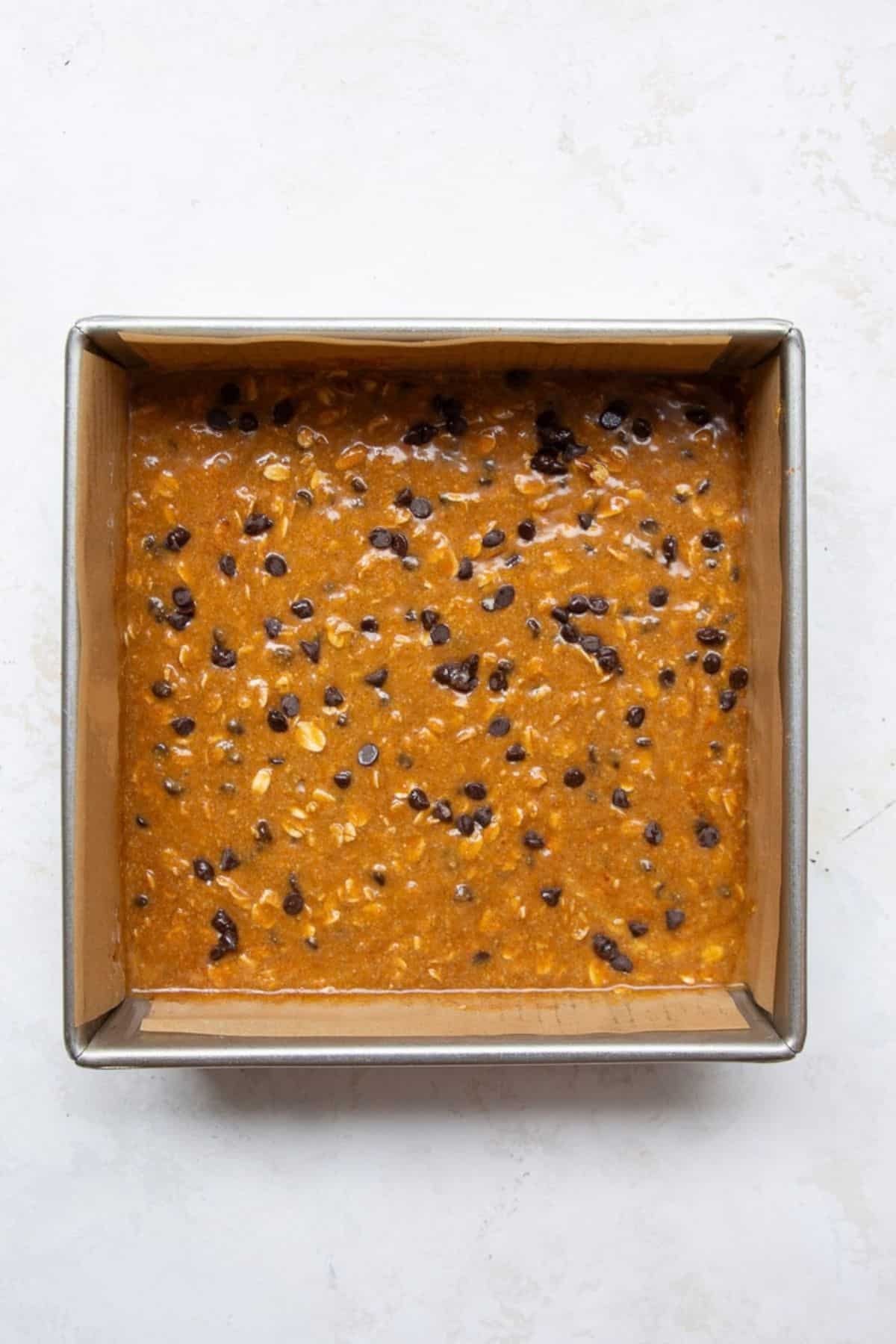 Pumpkin oatmeal bar batter topped with chocolate chips in a lined 8x8 pan before baking.