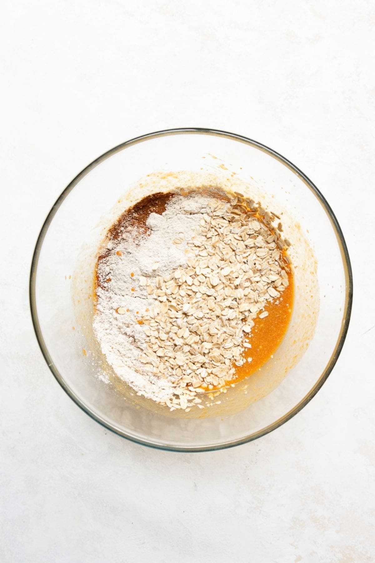 Oat flour, rolled oats, and pumpkin pie spice added to the wet ingredients in a glass bowl.