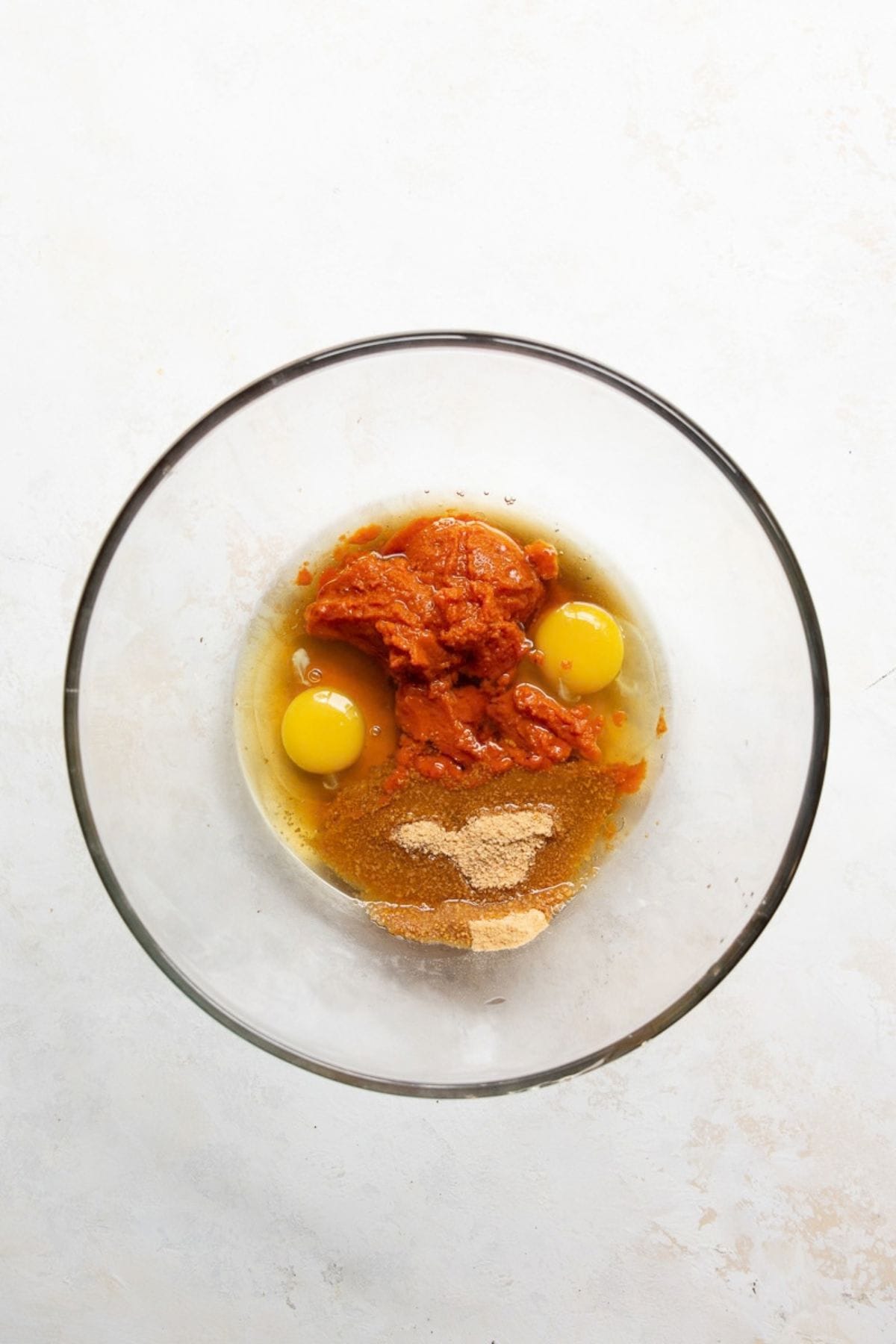 Eggs, pumpkin puree, coconut sugar, and maple syrup in a glass bowl before mixing.