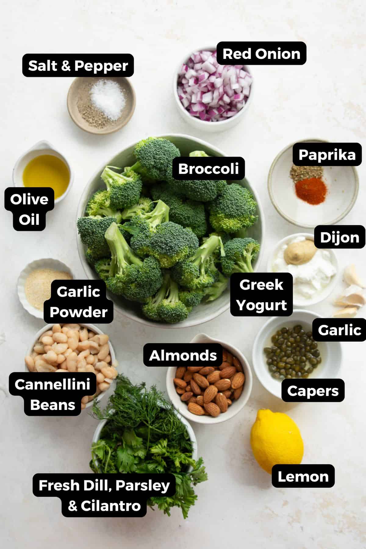 Labeled ingredients for roasted broccoli salad including broccoli, cannellini beans, almonds, fresh herbs, Greek yogurt, lemon, and capers.