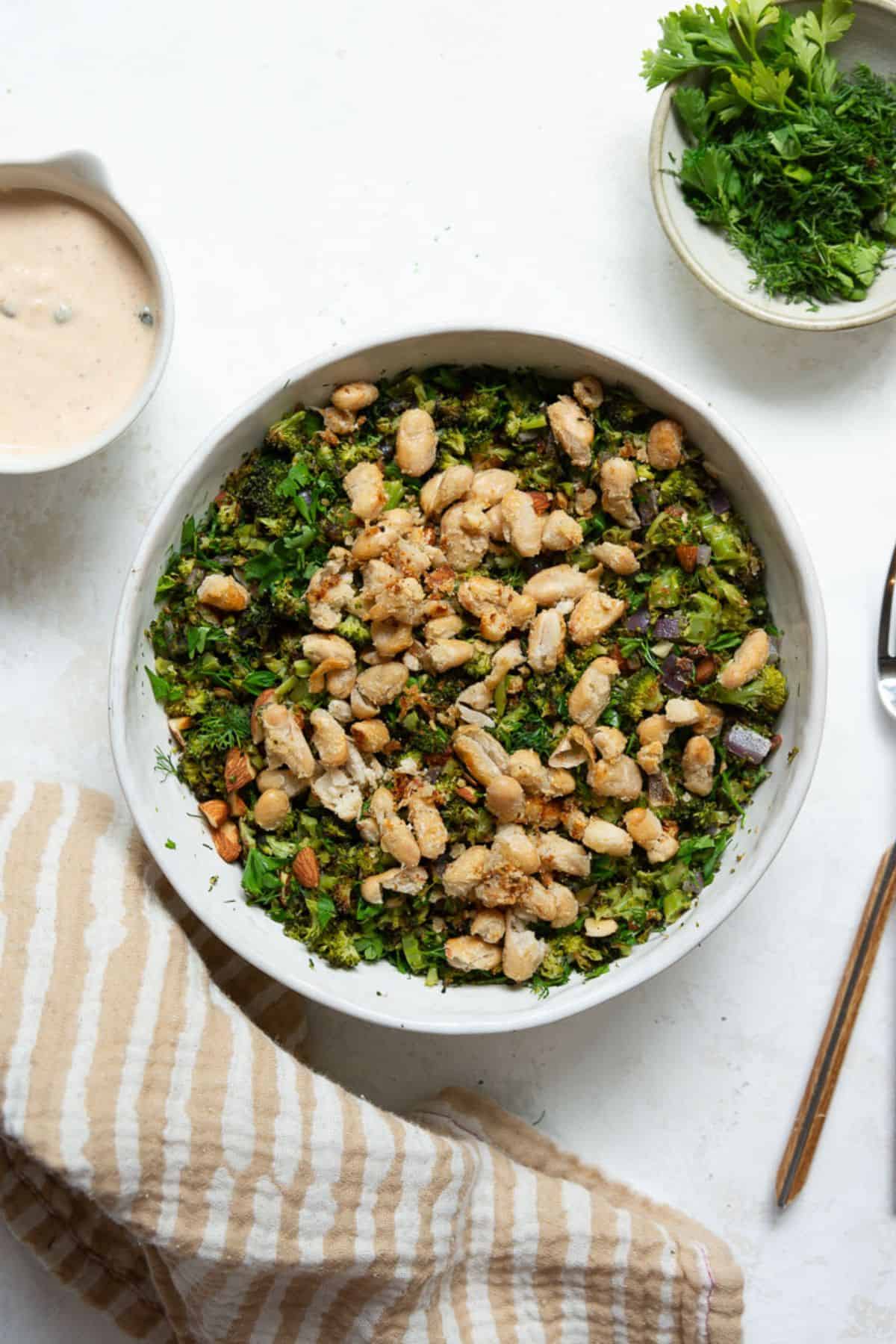 Roasted broccoli salad with fresh herbs and topped with crispy white bean crumble in a white bowl.