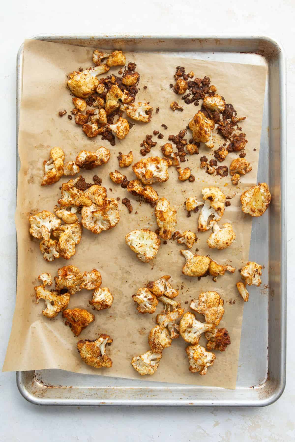 Spiced roasted cauliflower with golden brown edges on a parchment-lined sheet pan.