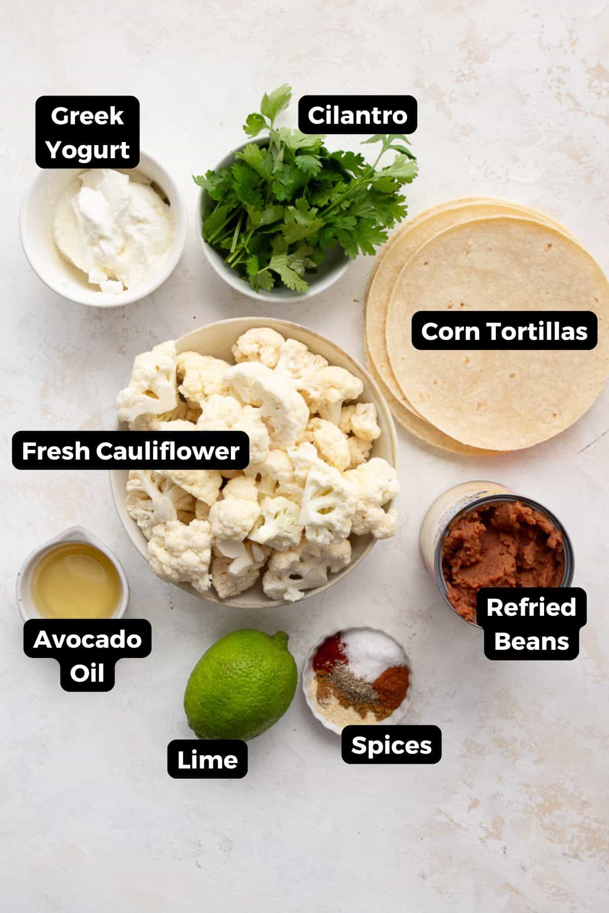 Ingredients for cauliflower tacos labeled: cauliflower florets, Greek yogurt, cilantro, corn tortillas, refried beans, avocado oil, lime, and spices.
