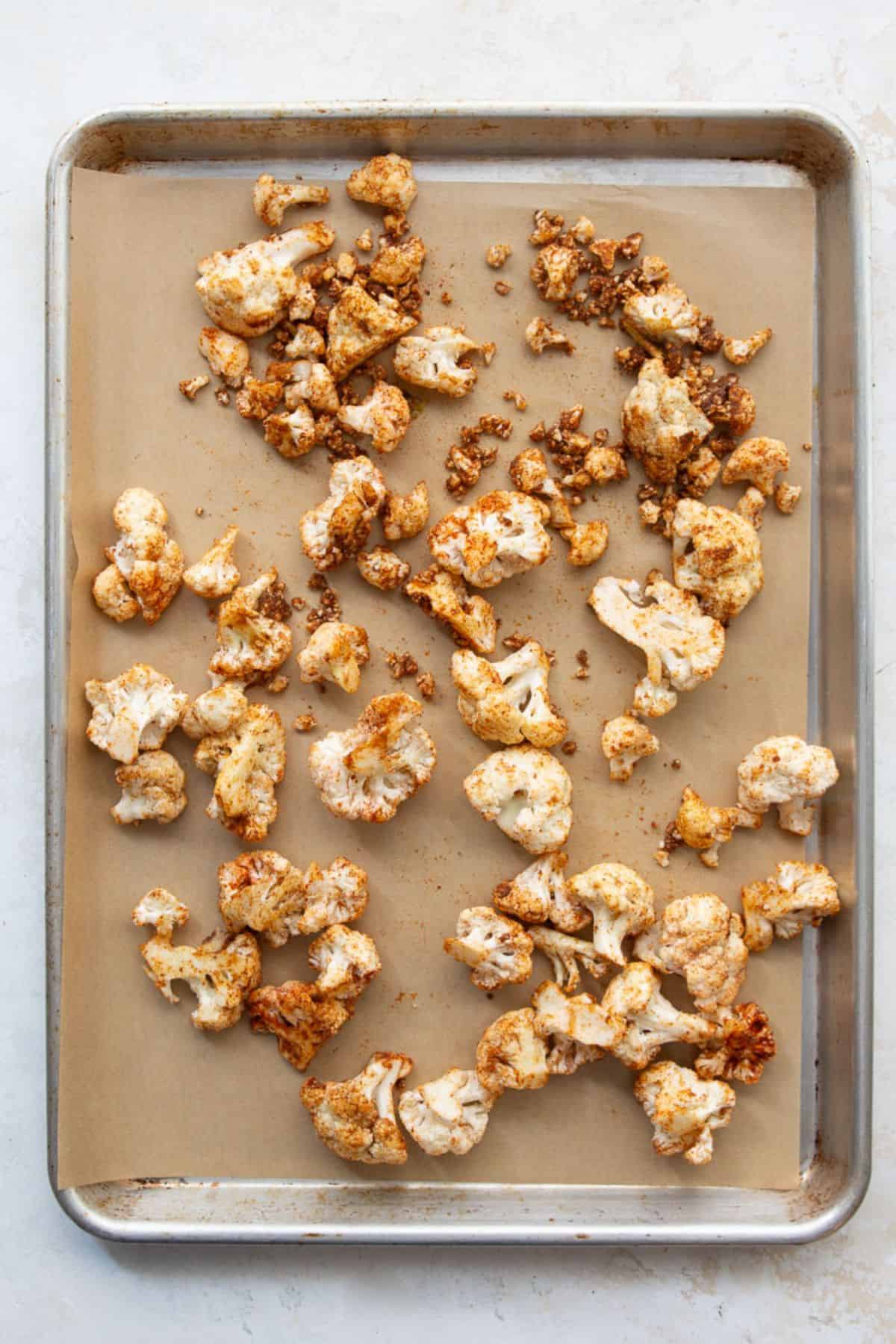 Seasoned raw cauliflower florets spread in a single layer on a parchment-lined baking sheet.