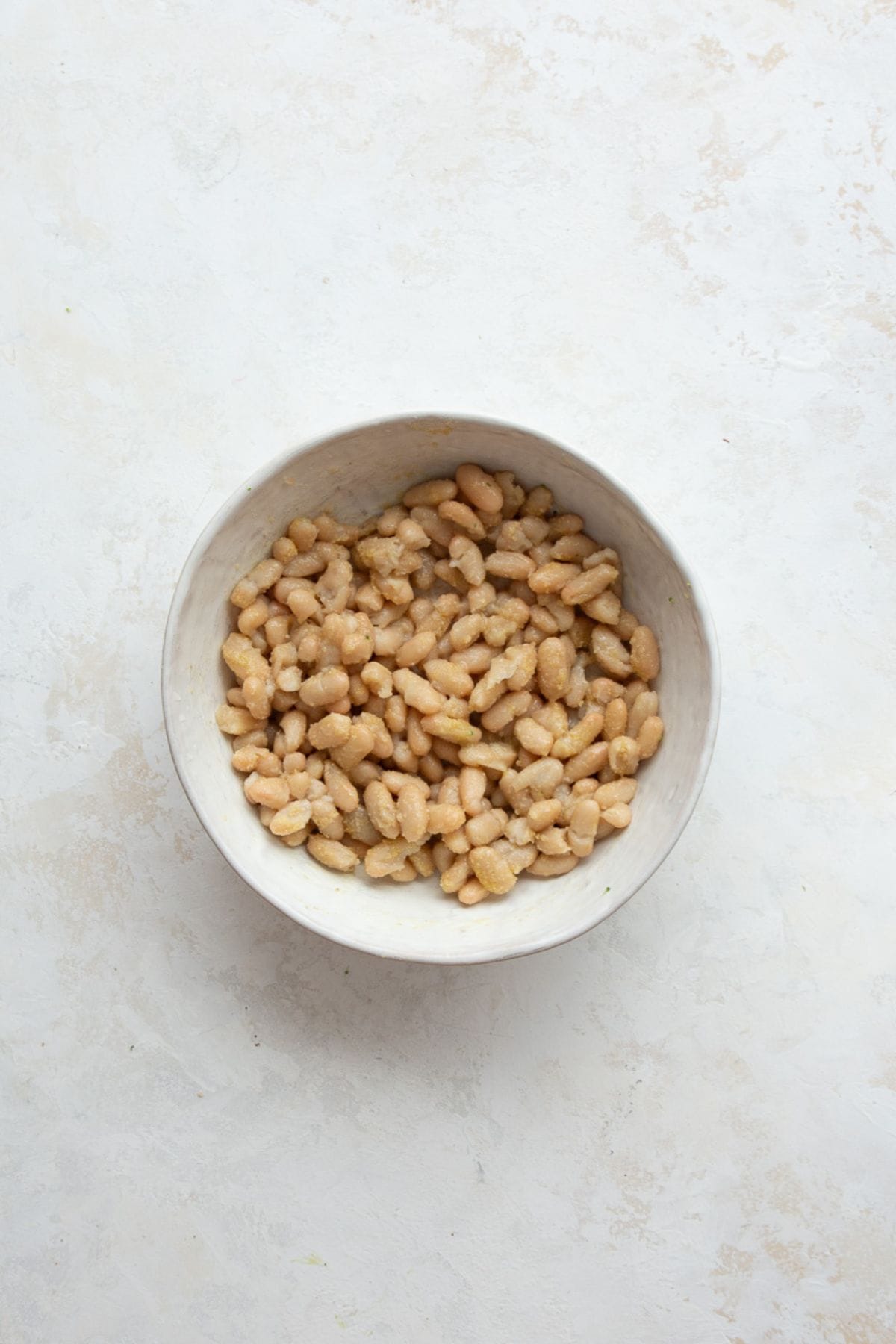 Cannellini beans tossed with olive oil and seasoning in a white bowl.