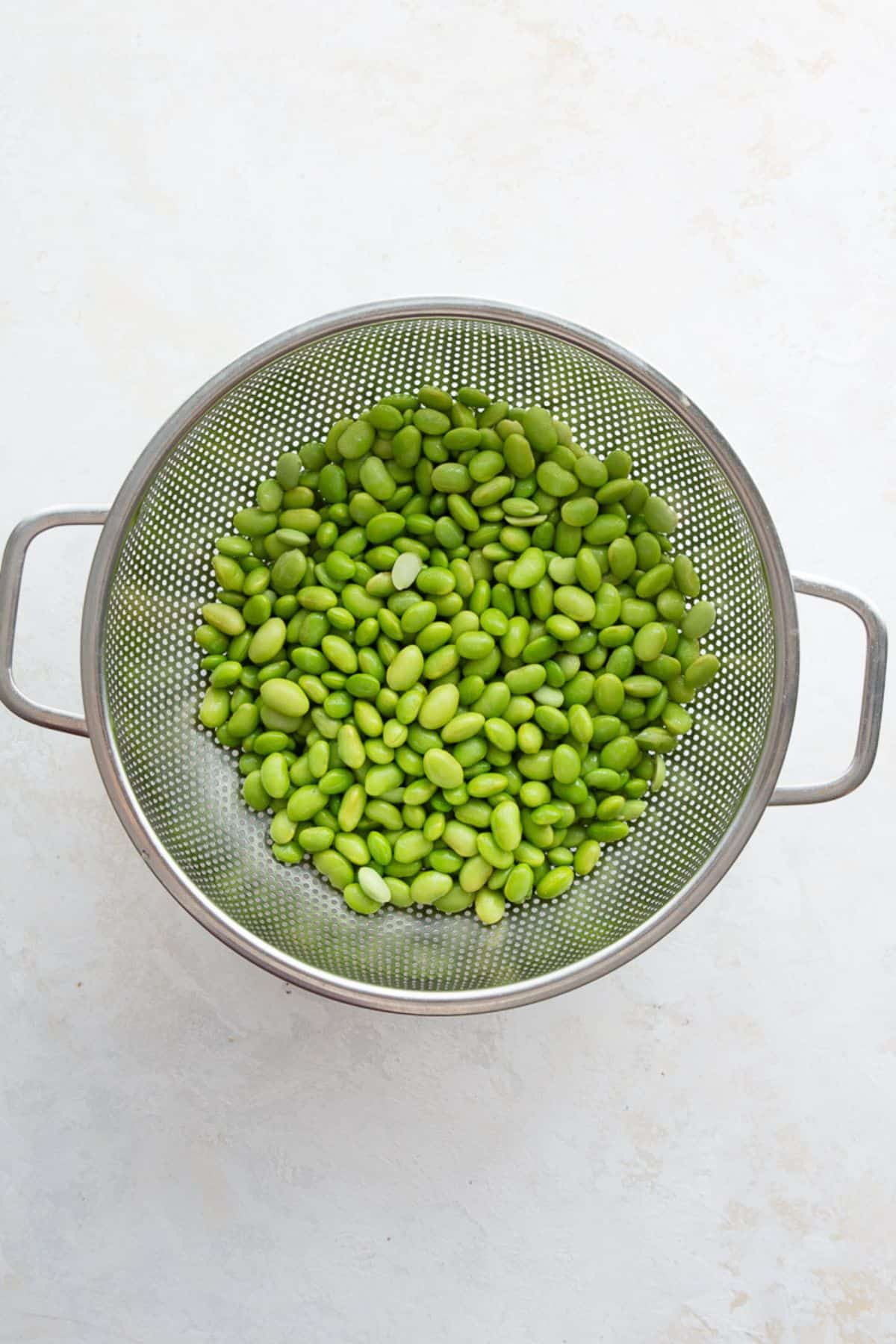 Thawed shelled edamame draining in a metal colander.