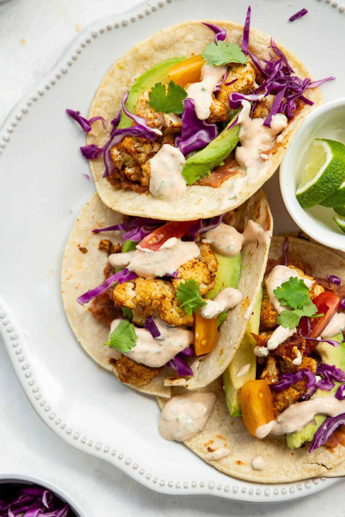 Roasted cauliflower tacos with refried beans, avocado, red cabbage, and cilantro yogurt crema.