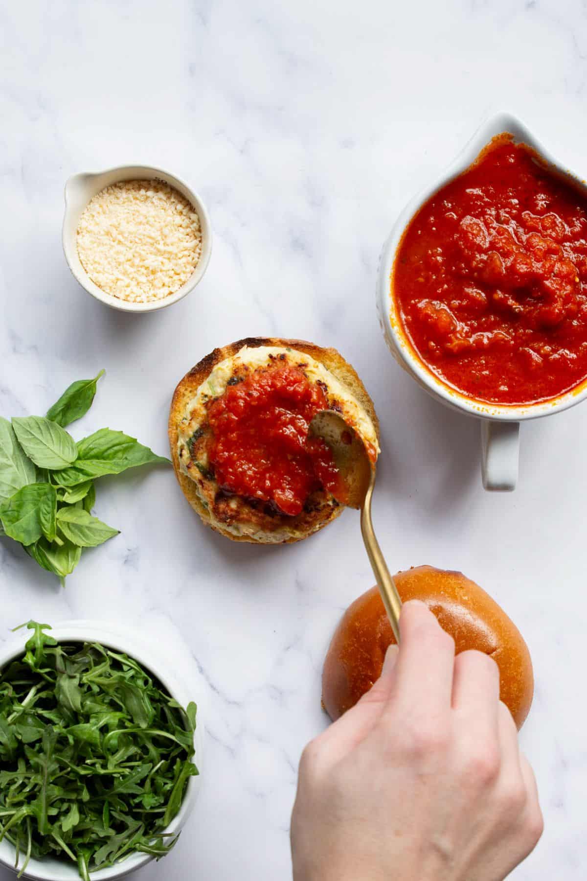 Spooning marinara onto a chicken parm burger.