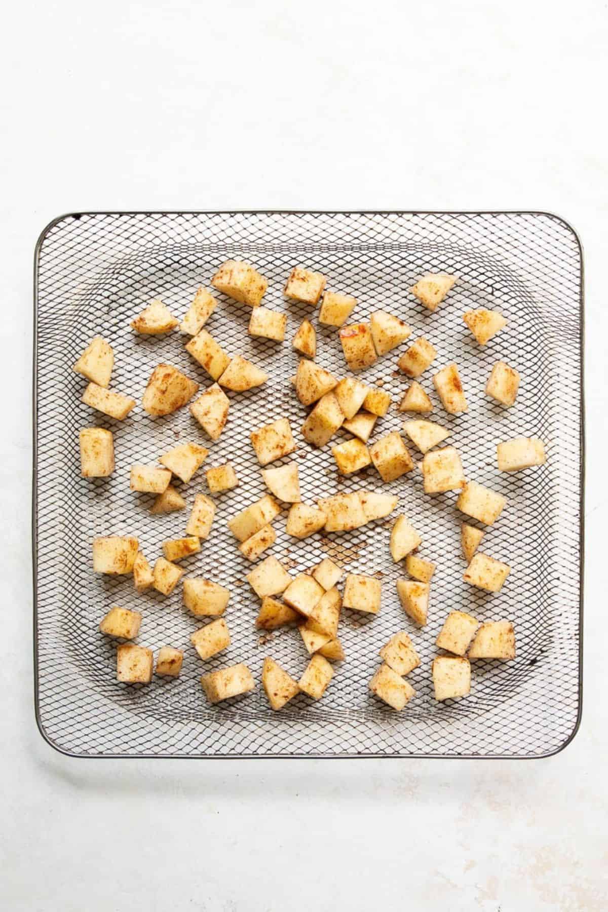 Cinnamon-coated apple cubes spread in a single layer in an air fryer basket before cooking.