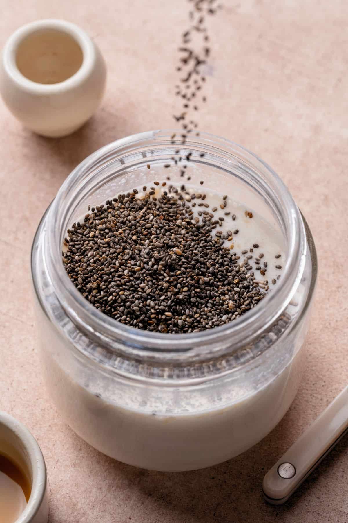 Chia seeds being poured into coconut milk, yogurt, and collagen in a glass jar.