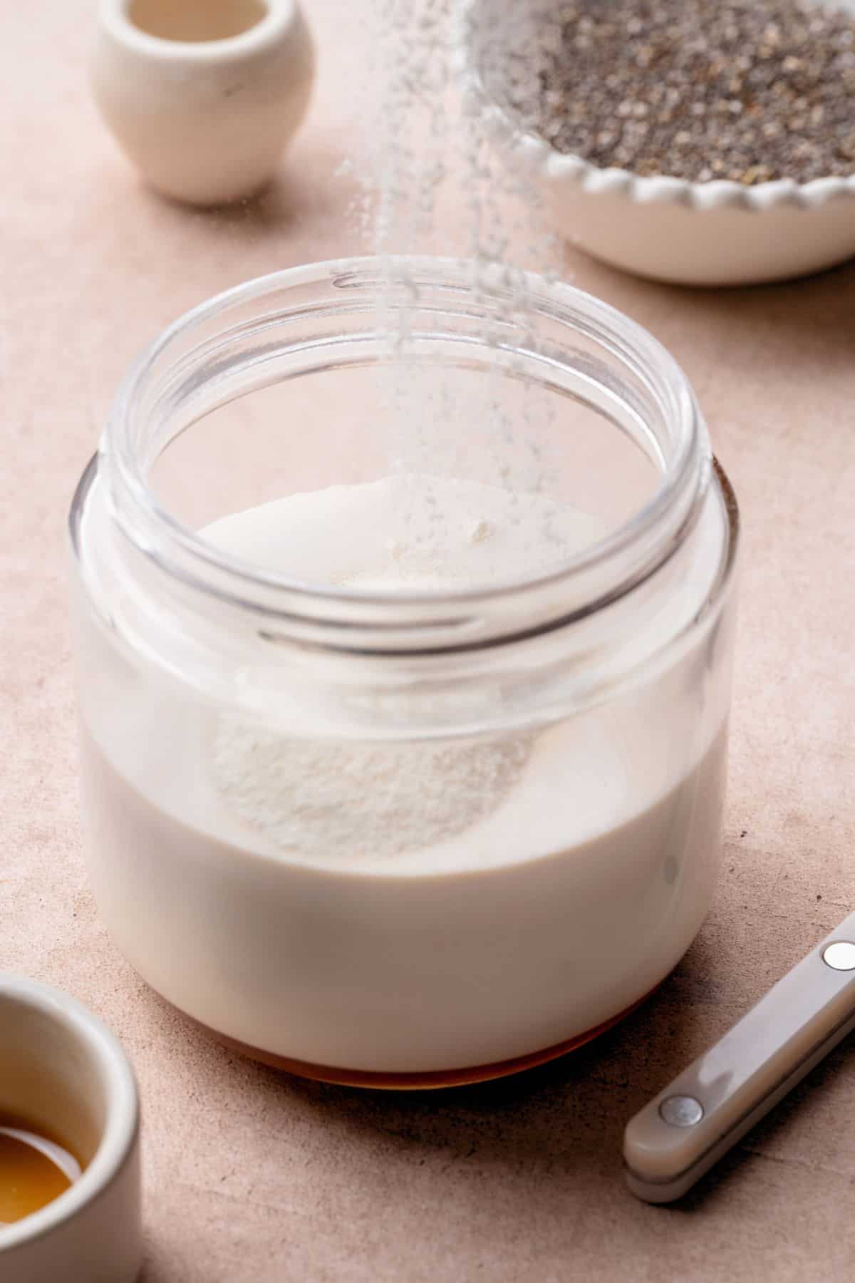 Collagen powder being sprinkled into coconut milk for high protein chia pudding.