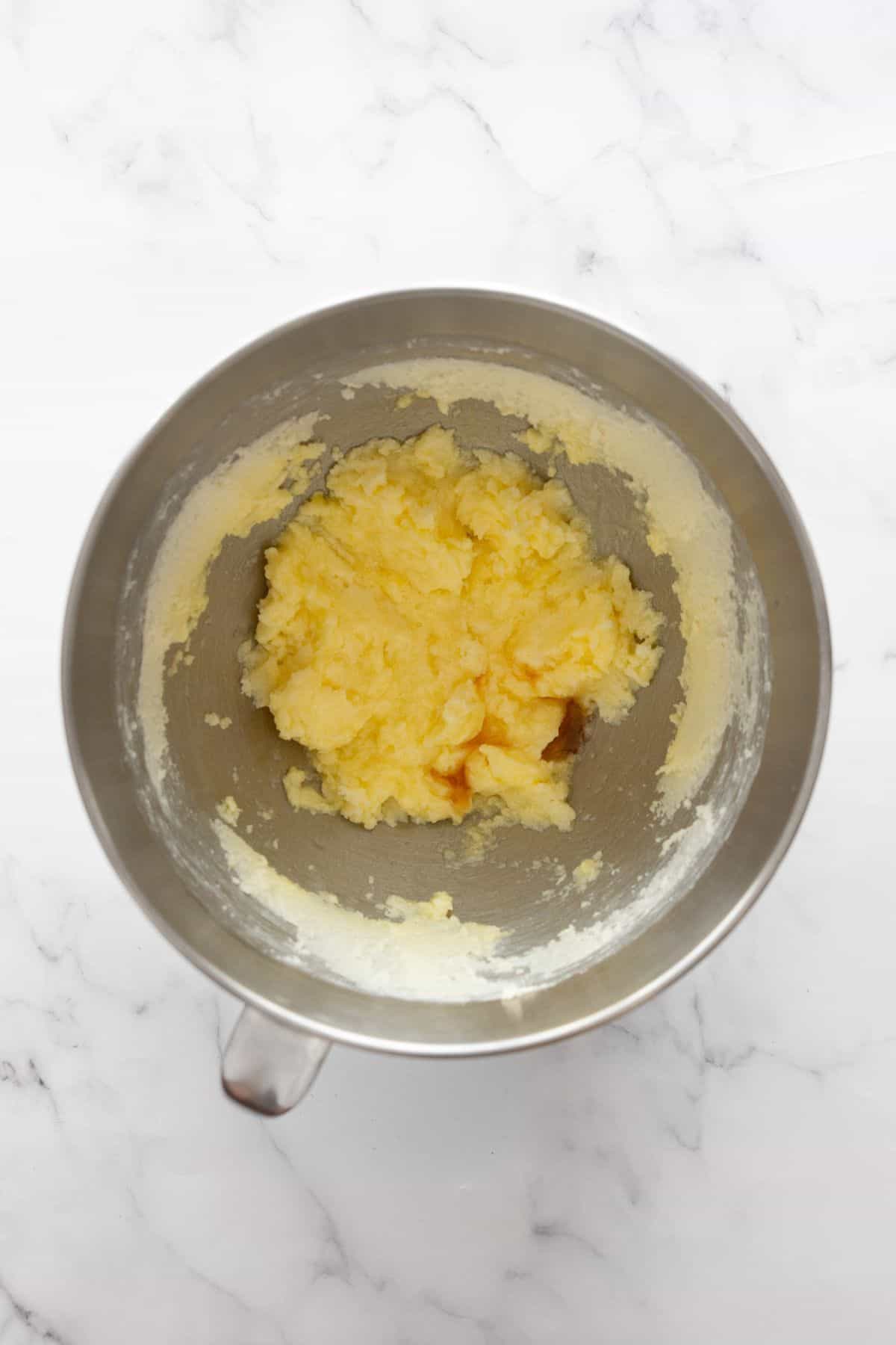 Maple syrup, vanilla, egg, and egg yolk mixed into creamed butter and sugar in a mixing bowl.