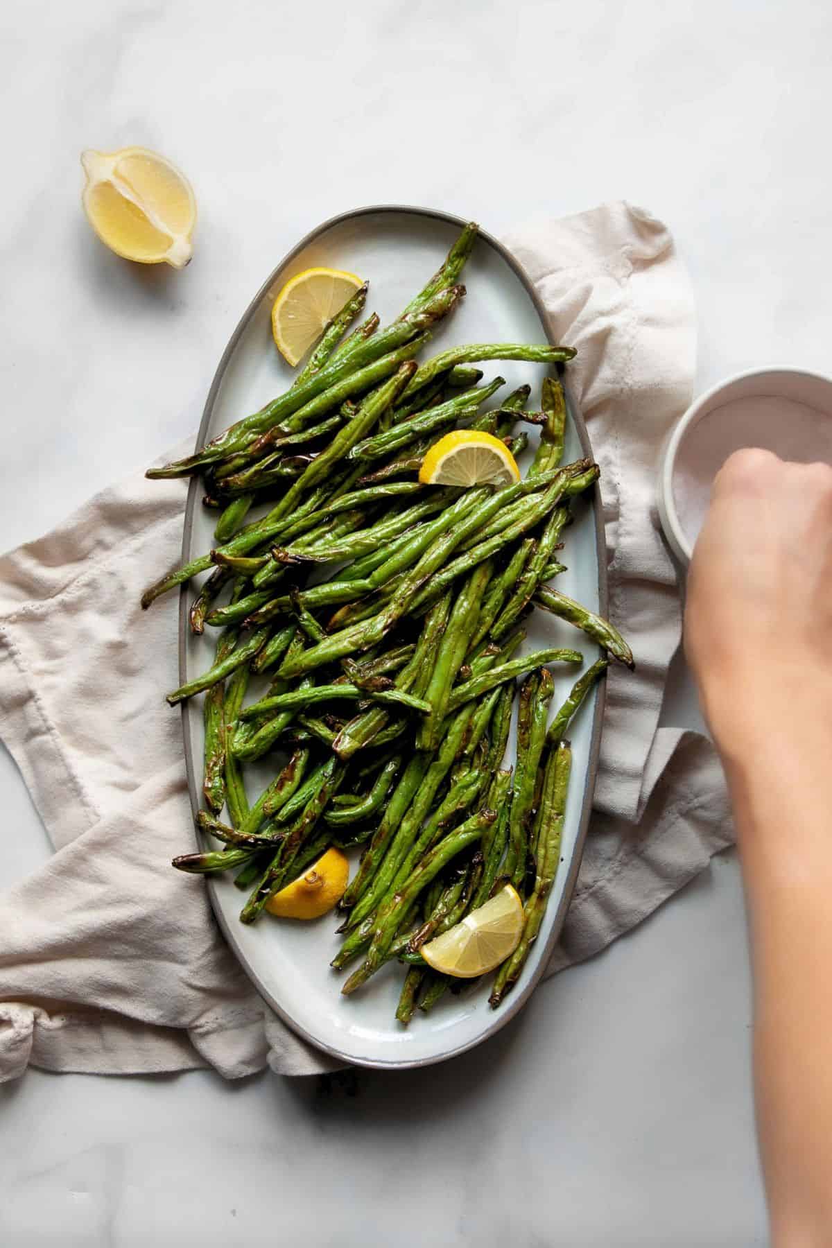 Air fryer green beans served on a platter with fresh lemon wedges.