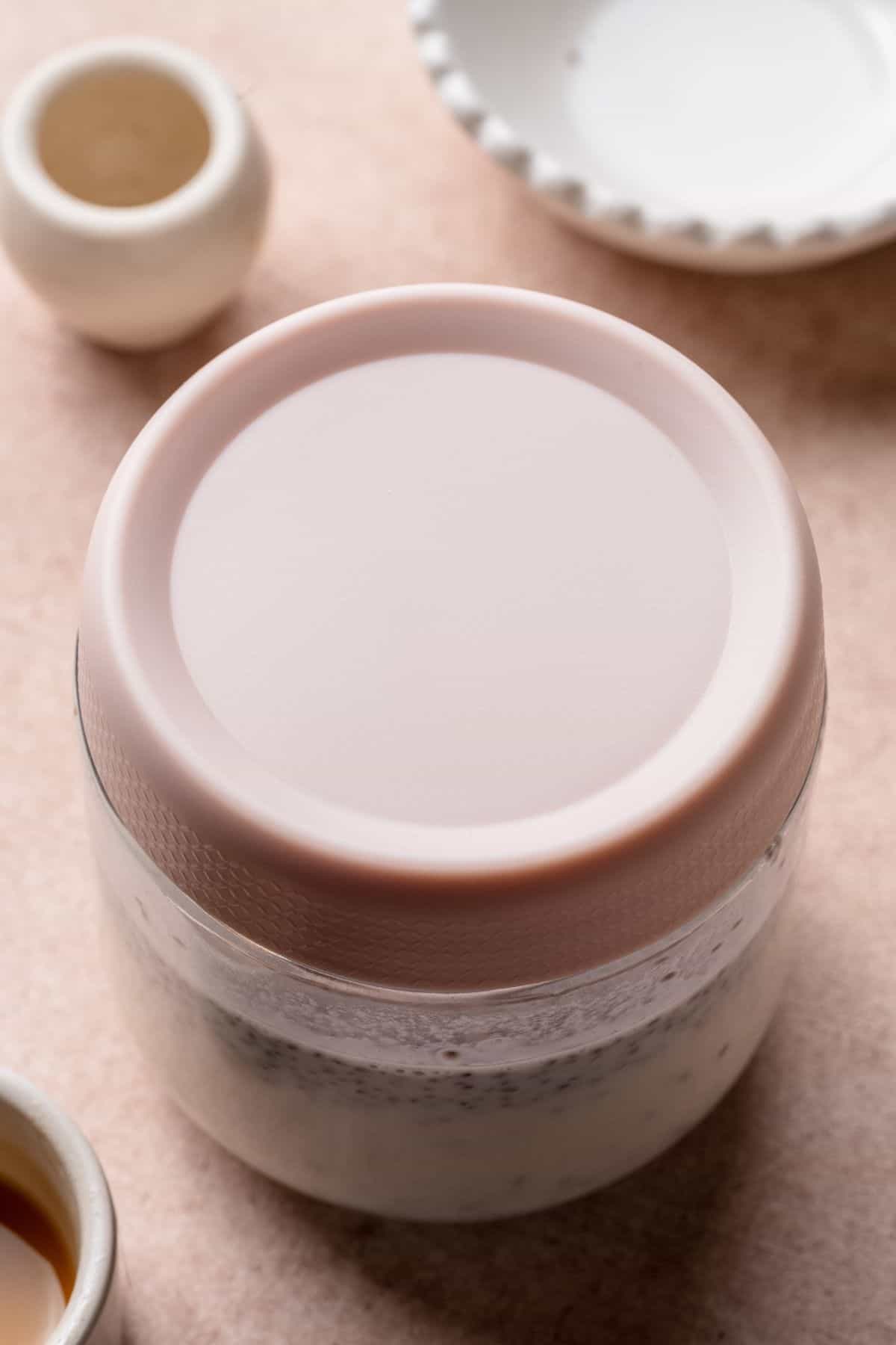 Glass jar of coconut chia pudding covered with a lid to chill in the fridge.
