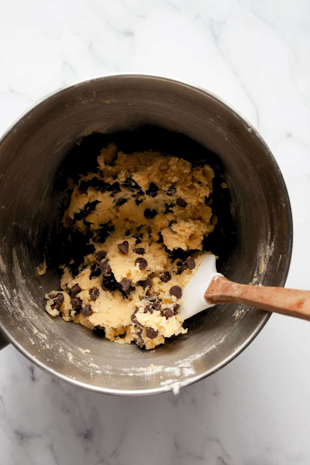 Folding chocolate chips into cookie dough with a wooden spatula.