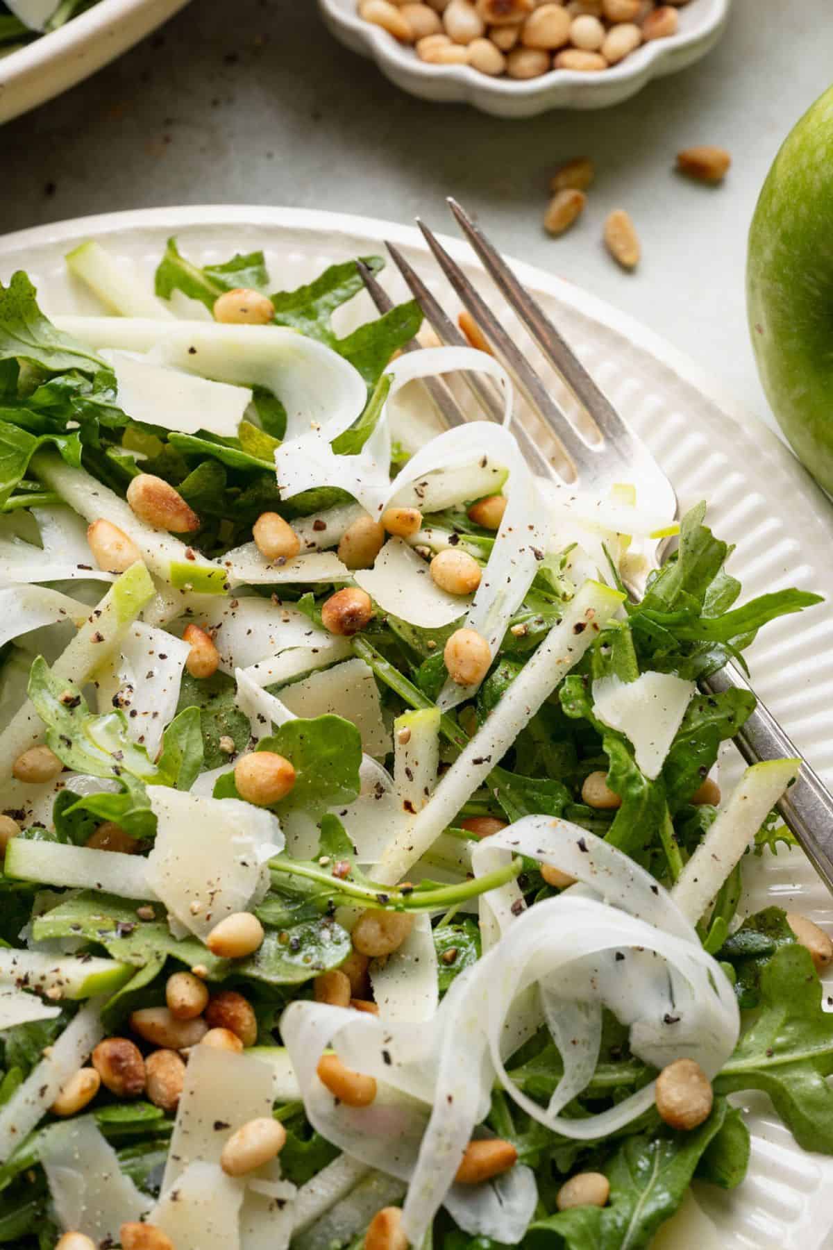 Close-up of shaved fennel salad with arugula, Granny Smith apple, Parmesan, pine nuts, and black pepper.