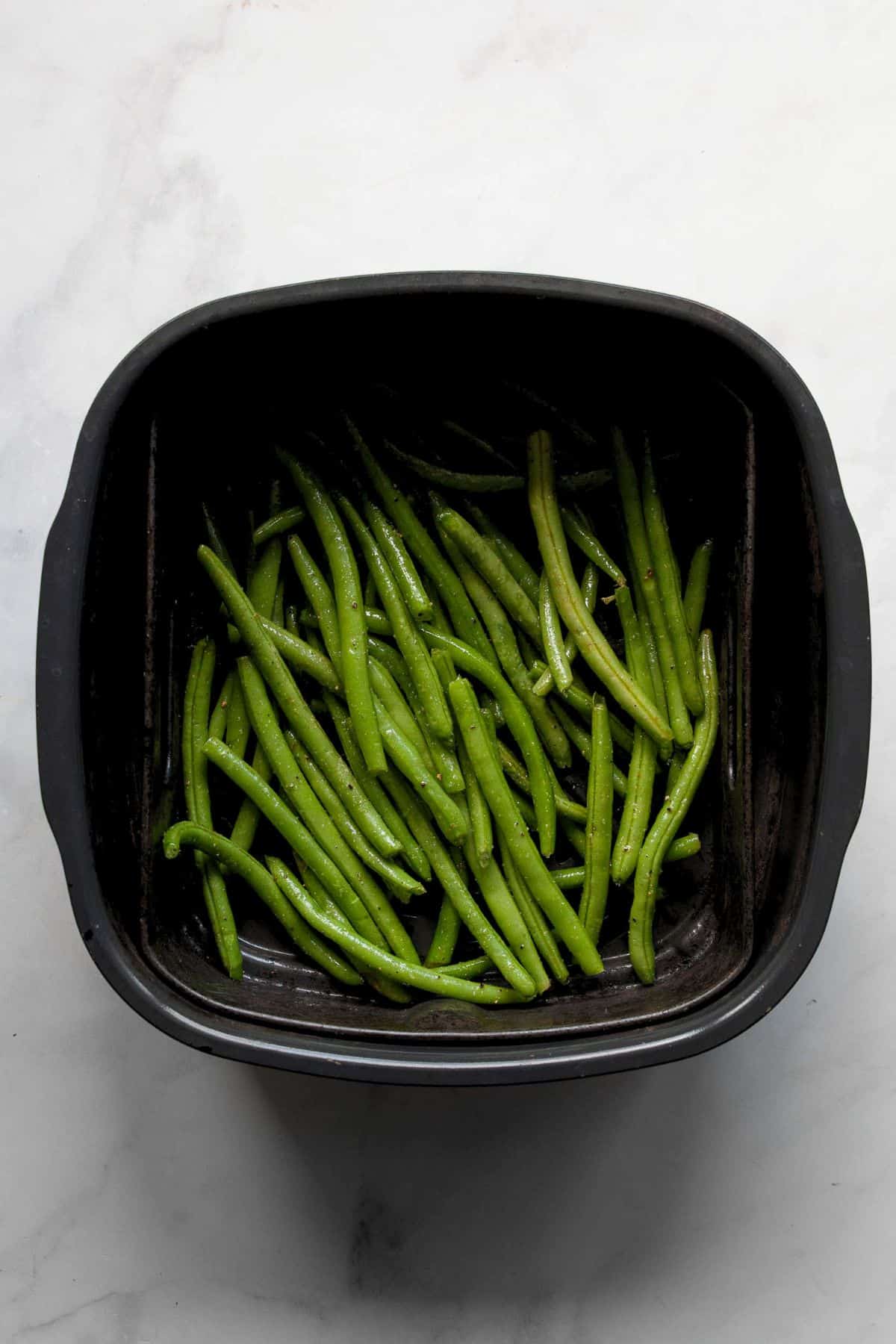Air fried green beans with blistered, browned spots in the air fryer basket.