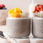 High protein coconut milk chia pudding in glass jars topped with mango, berries, granola, and shredded coconut.
