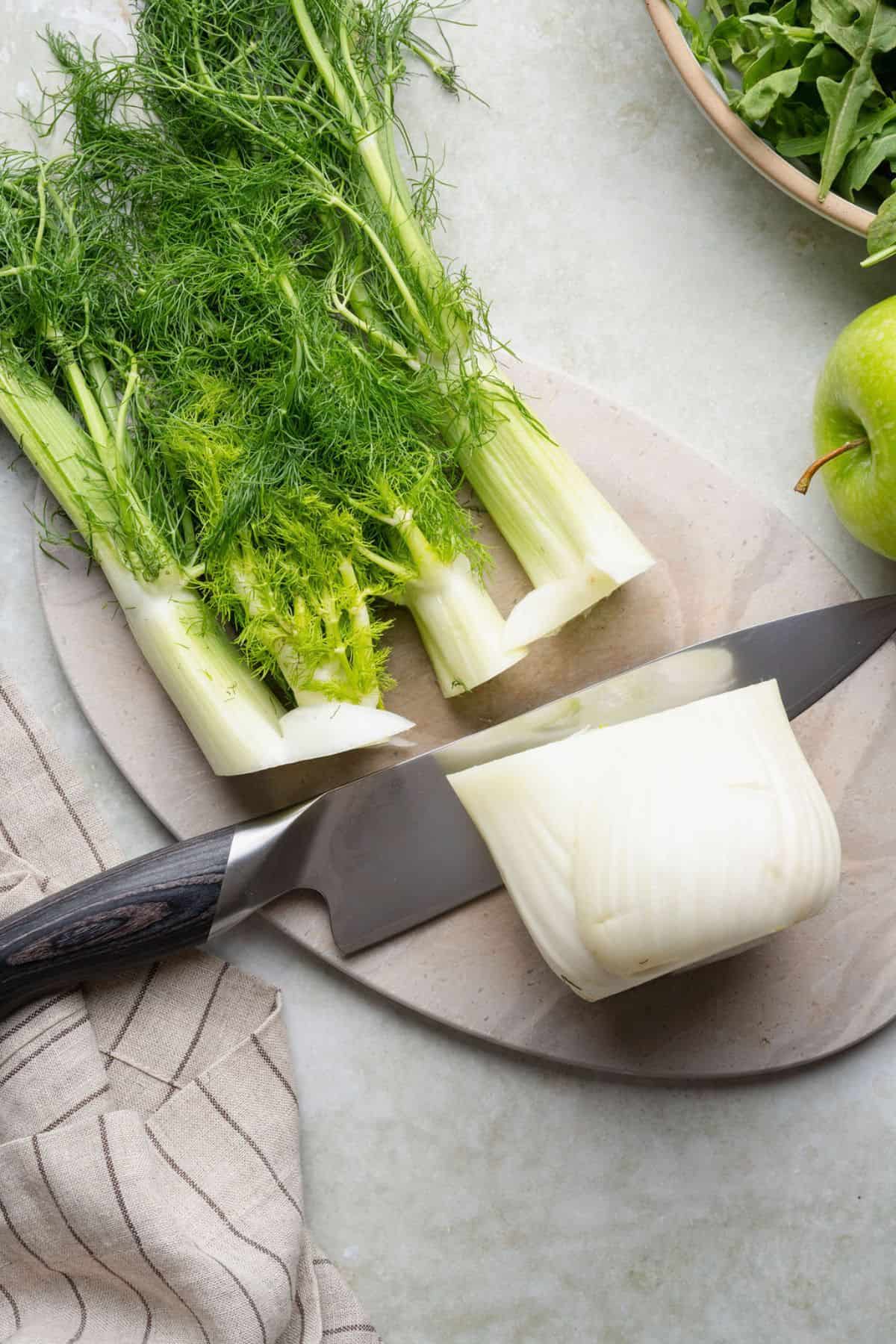 Trimming the stalks and fronds off a fennel bulb with a chef's knife.