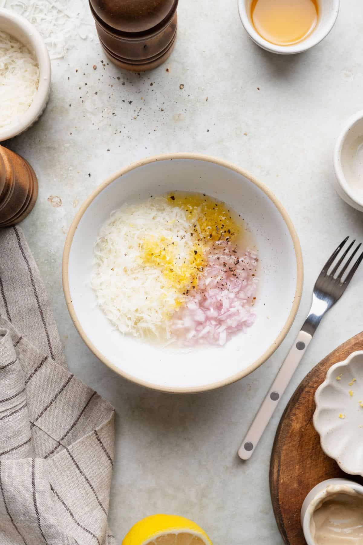 Combining grated Parmesan, lemon zest, lemon juice, shallot, and pepper to start the lemon Parmesan dressing.