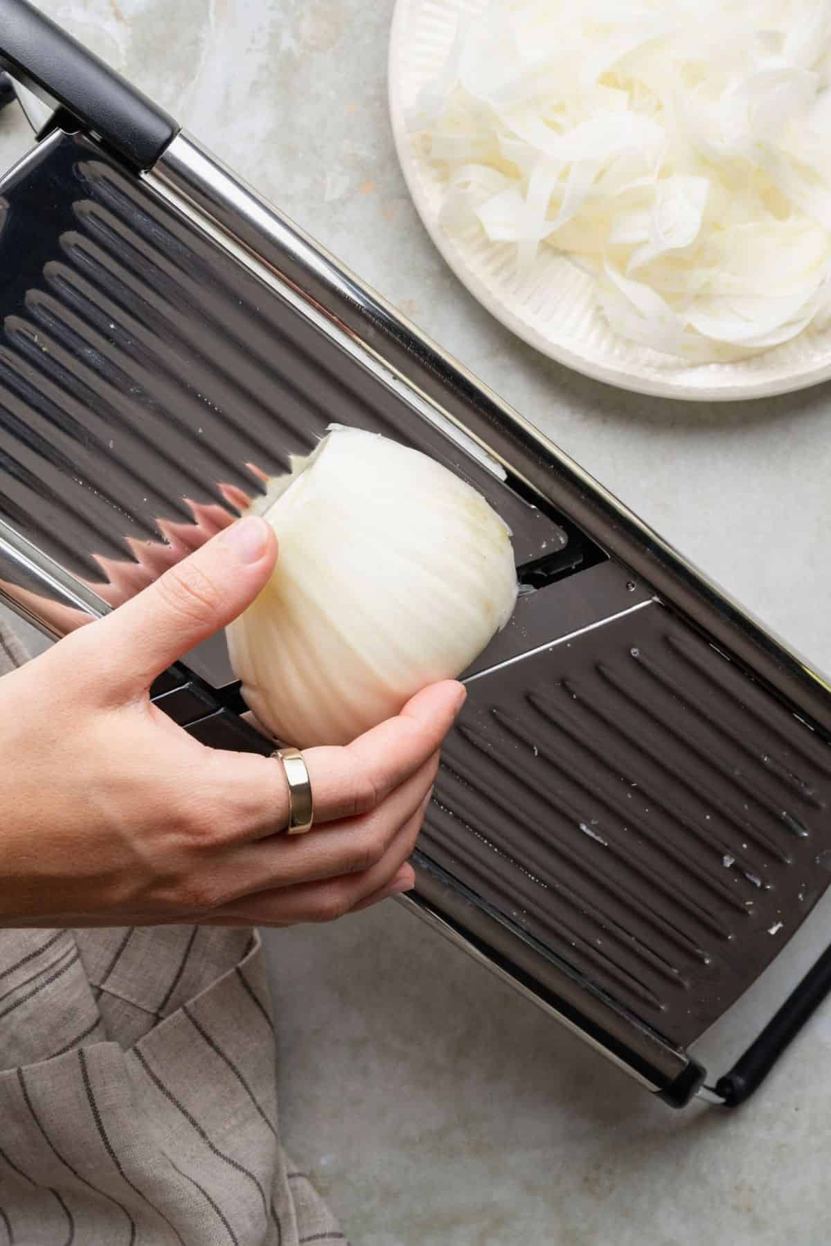 Shaving a cored fennel bulb half on a mandoline for fennel salad.