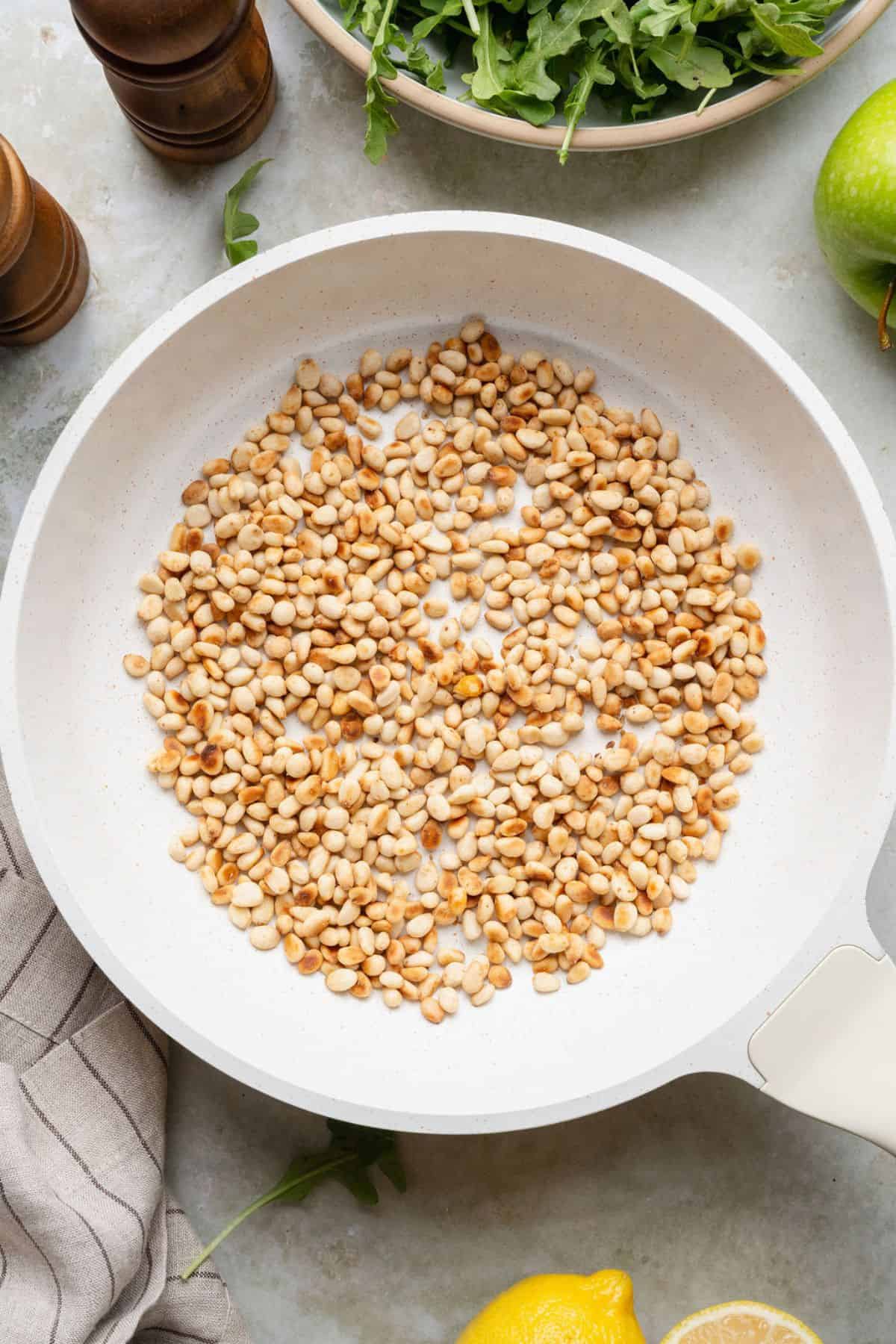 Toasting pine nuts in a dry skillet until golden for fennel salad.