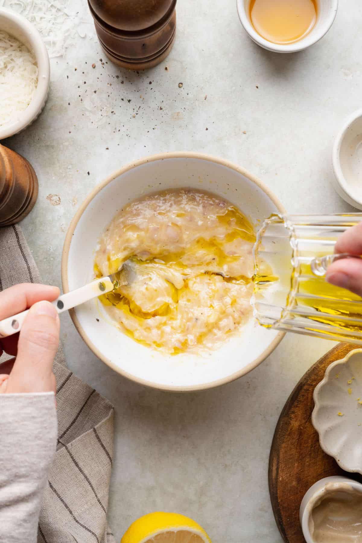 Slowly streaming olive oil into the lemon Parmesan dressing while whisking.